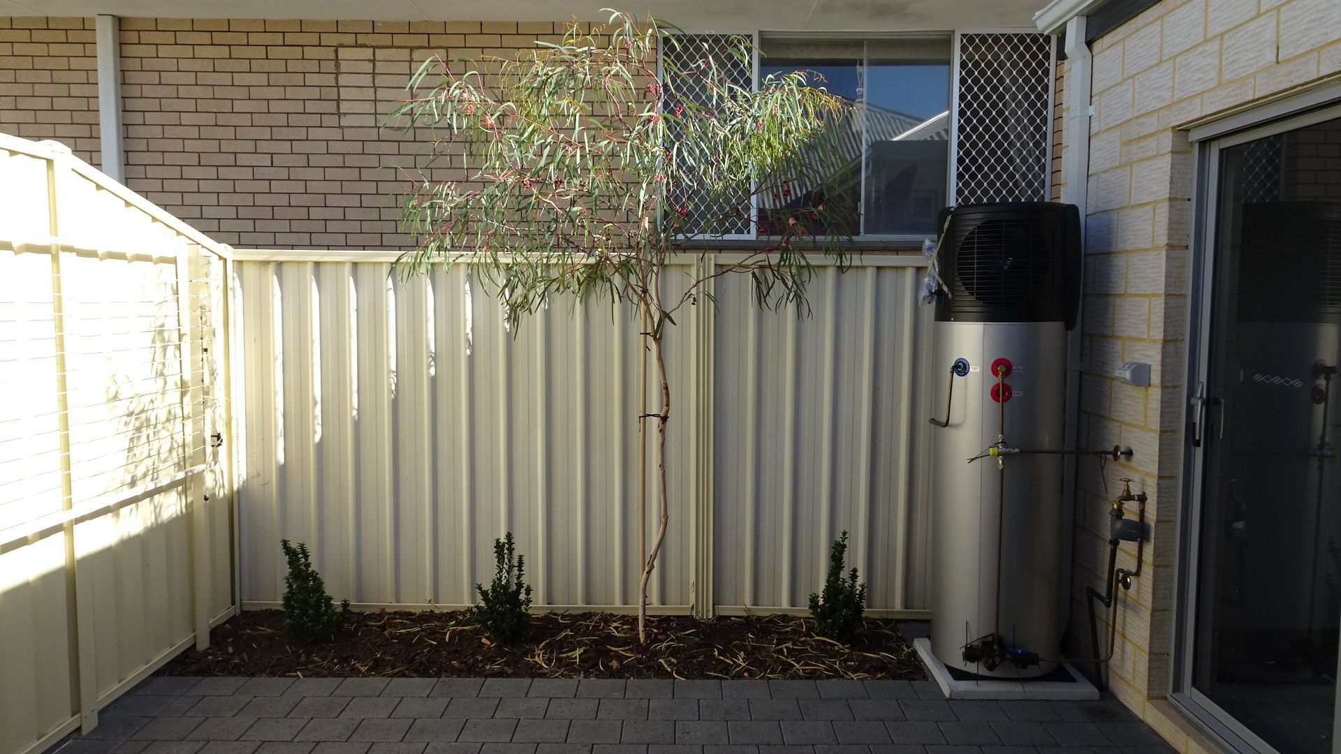 Courtyard with a tree, white fence, and a water heater next to a sliding glass door.