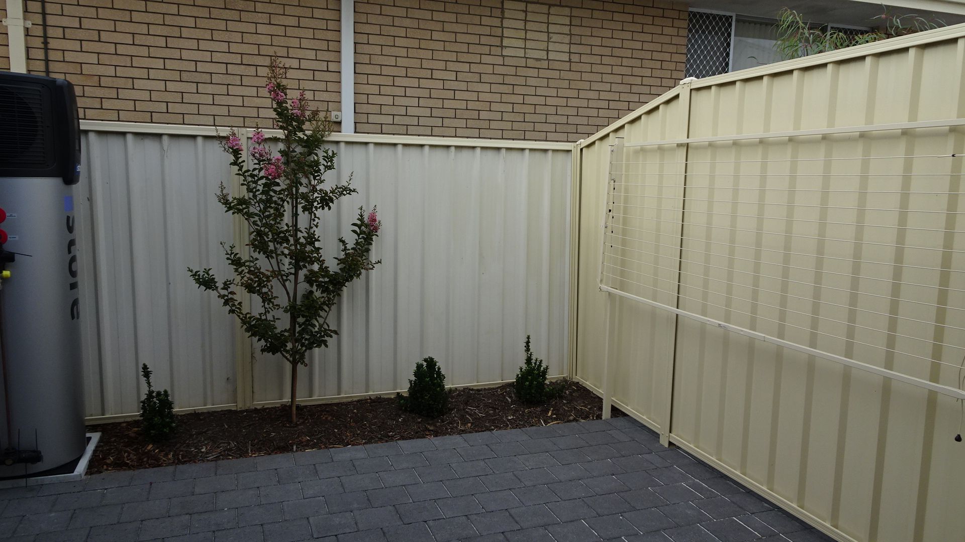 Small backyard with a cream-colored metal fence, gravel ground, and a small tree.