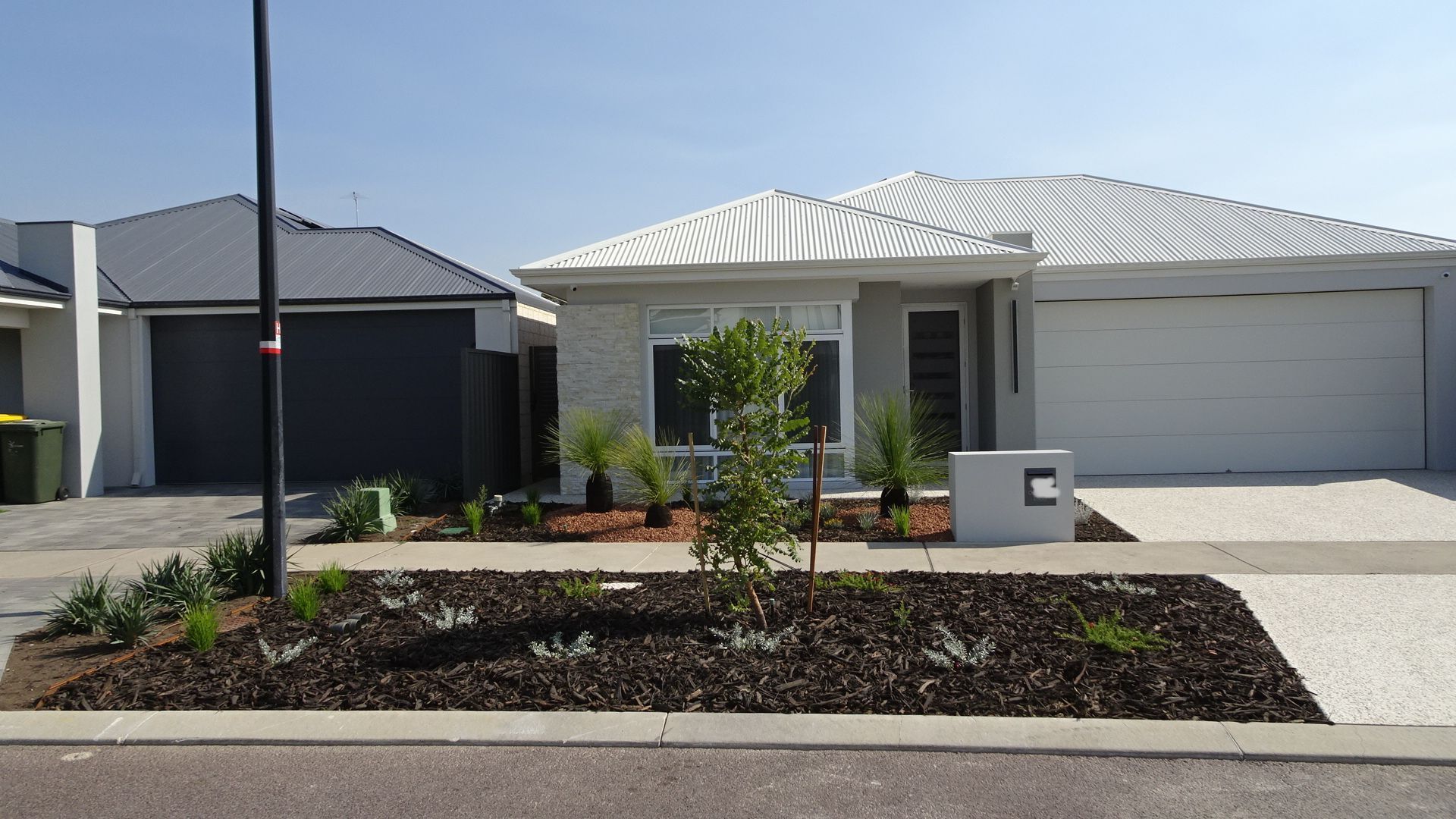 Two modern homes with gray and white exteriors, front yards with plants, and driveways, on a sunny day.