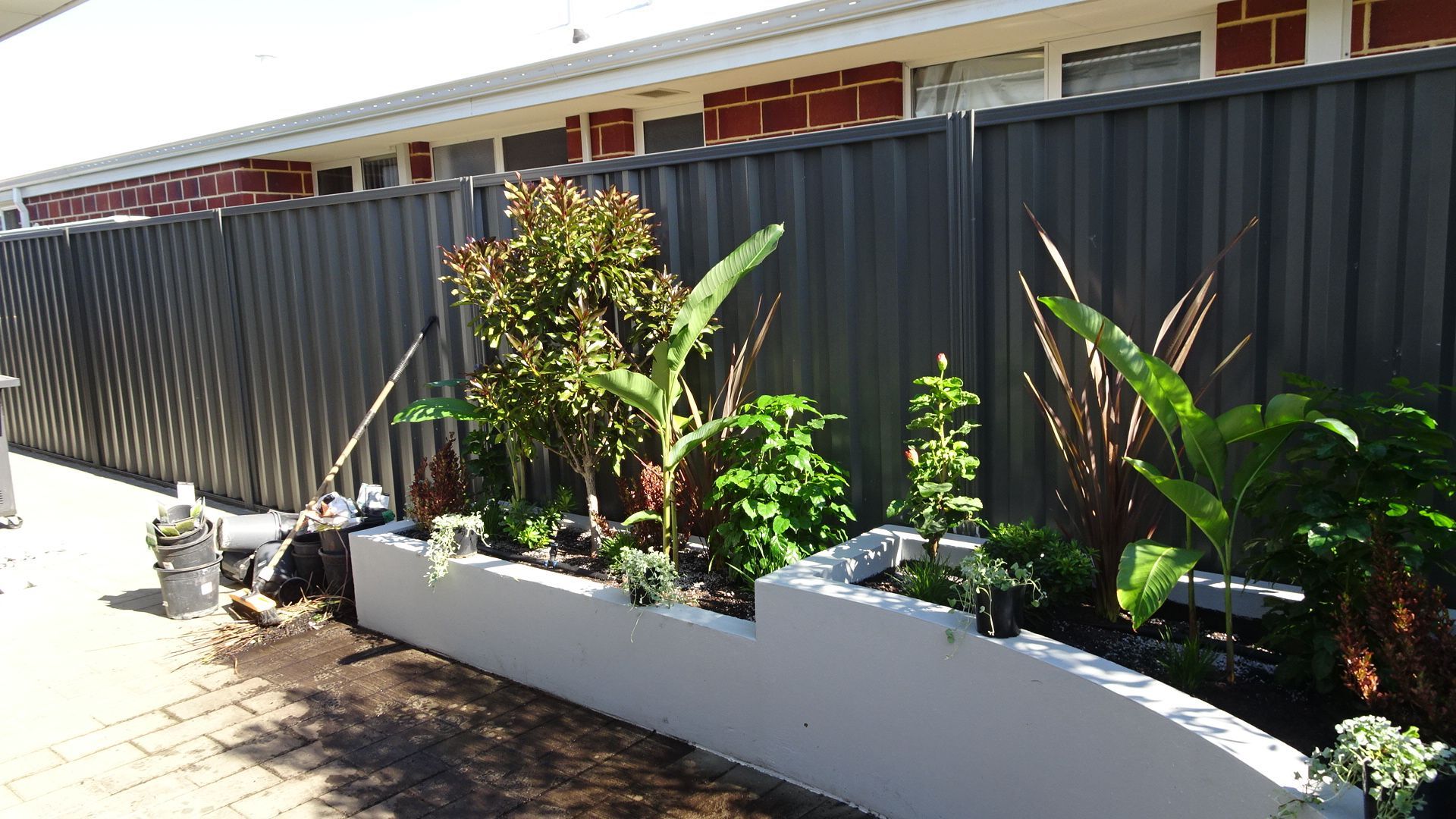 Concrete planter box with lush green plants against a gray fence.