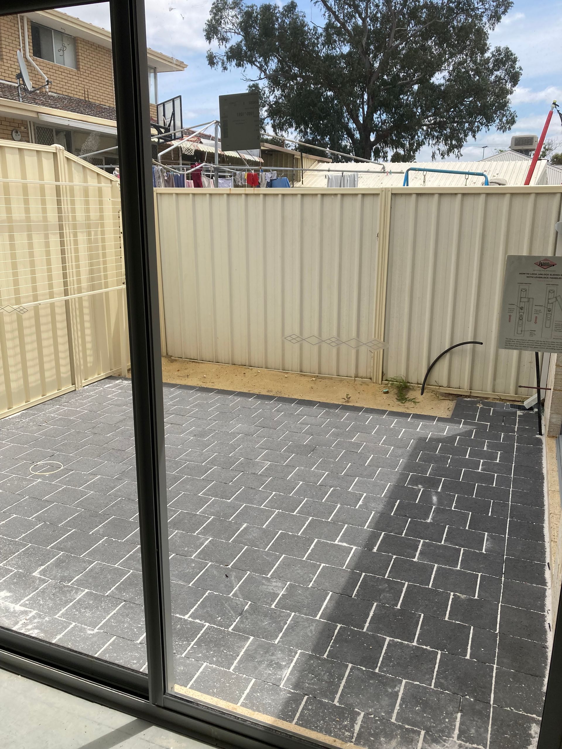 View from a sliding glass door of a paved backyard with a fence.