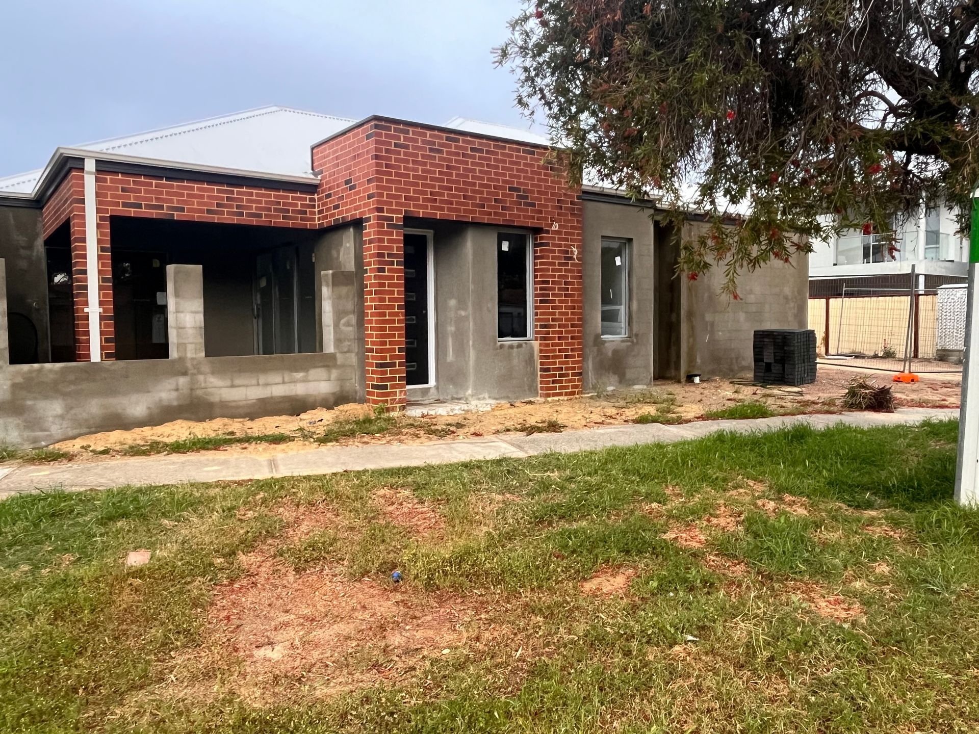 House under construction, red brick facade, gray stucco walls, lawn in front.