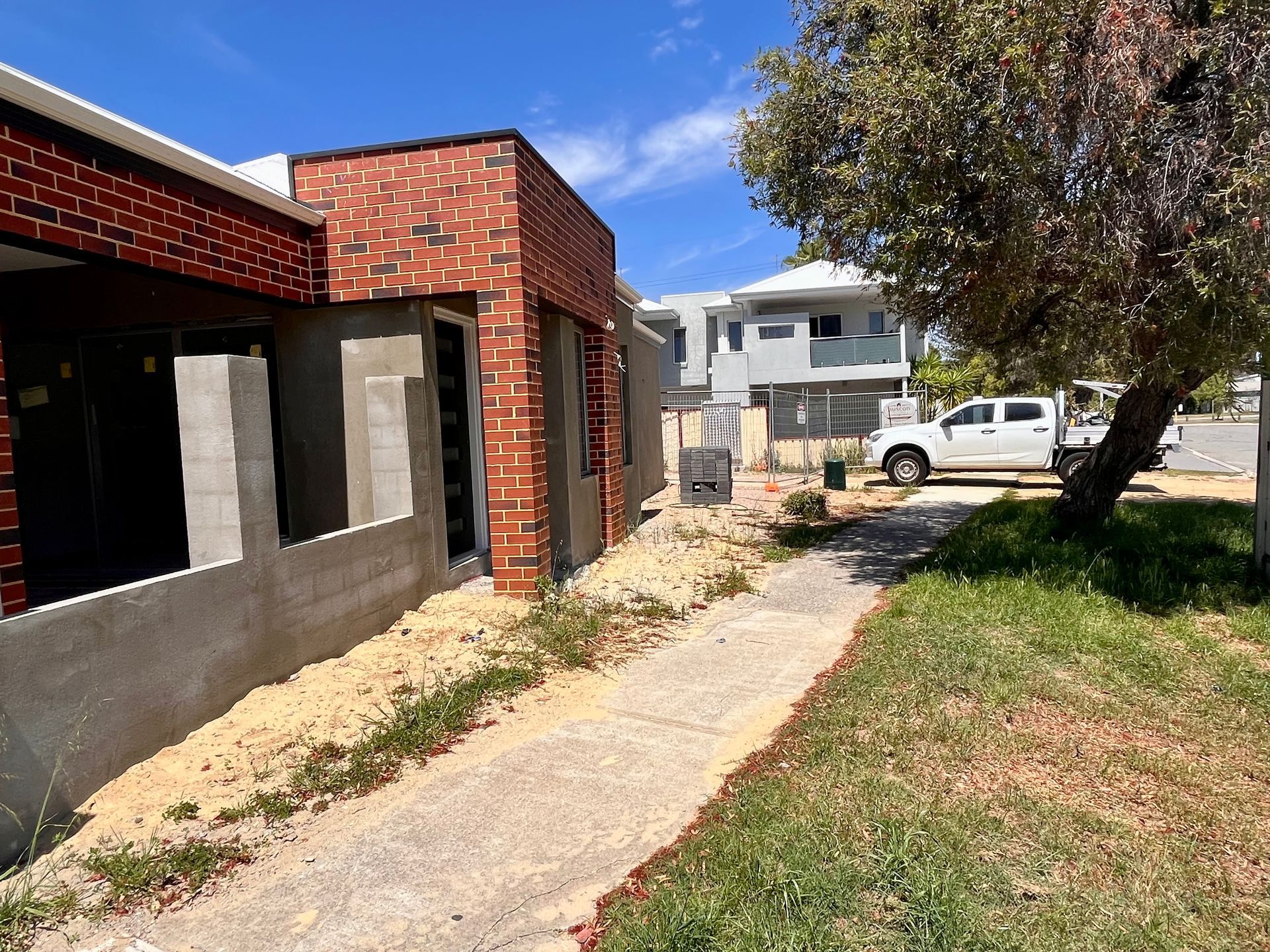 A building under construction with exposed brickwork, a sidewalk, and a white truck parked on the street.