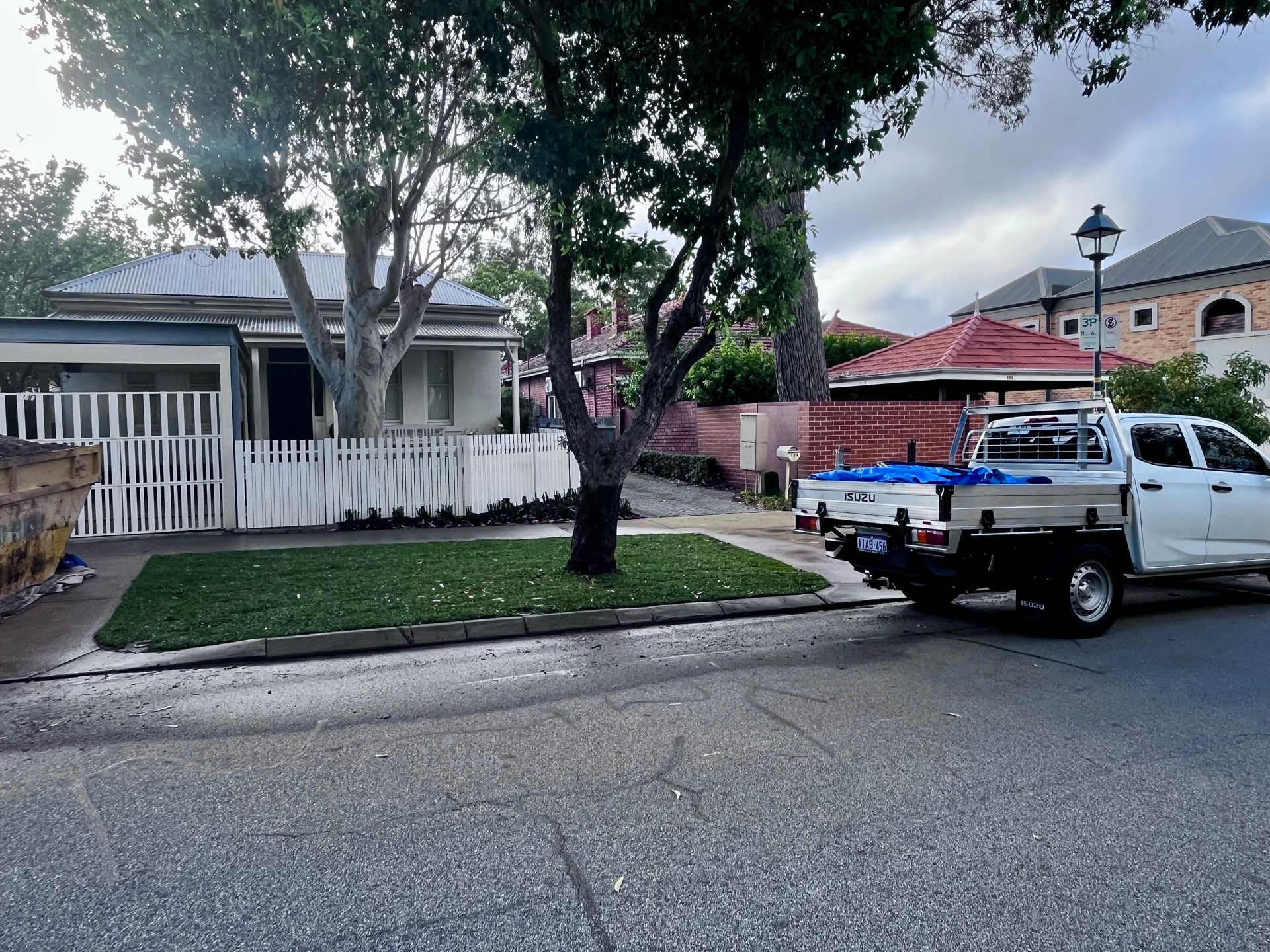 A white work truck parked on a street in front of houses with a grassy lawn and picket fence.