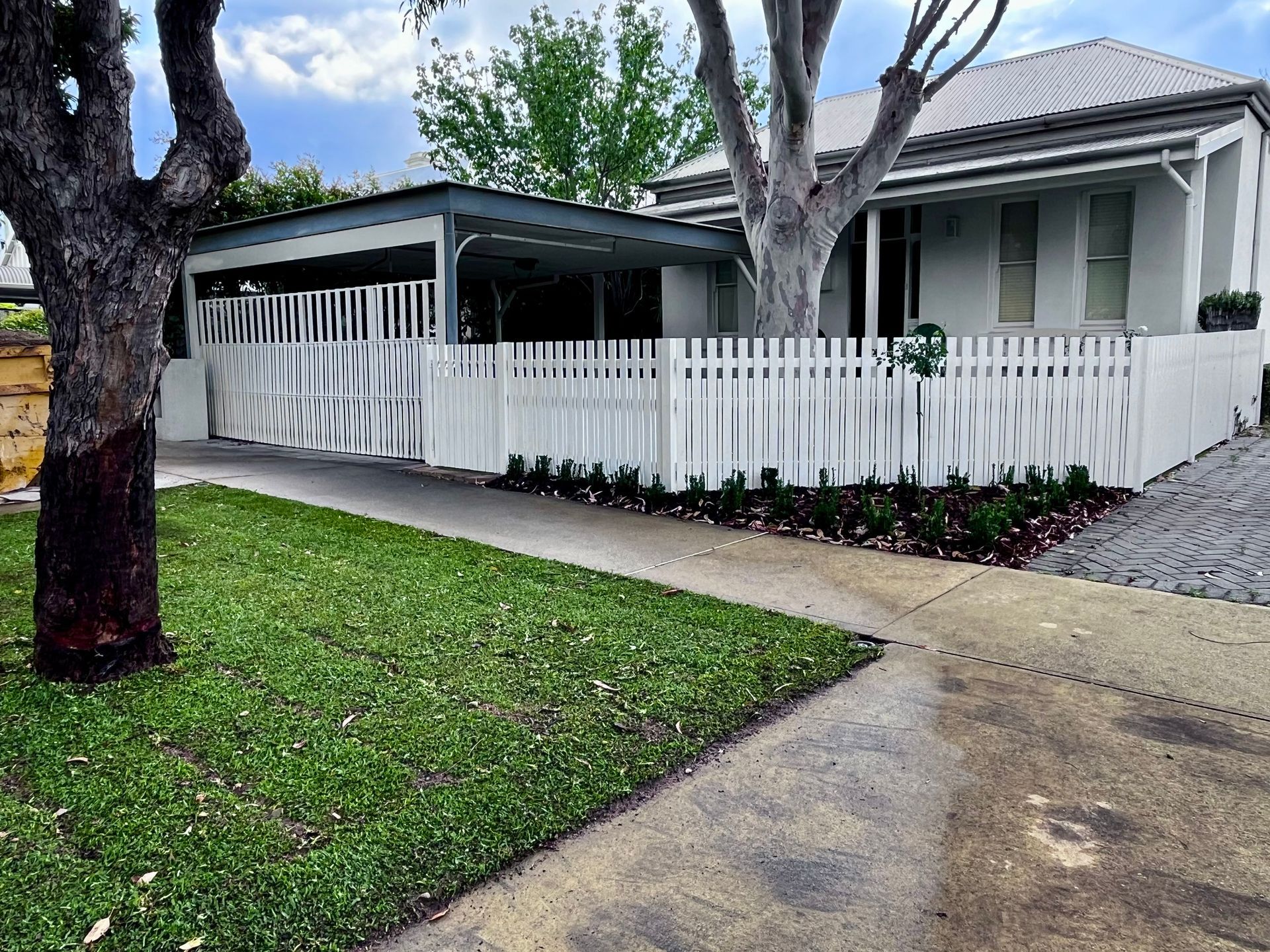 White house with a white fence, driveway, and front yard.