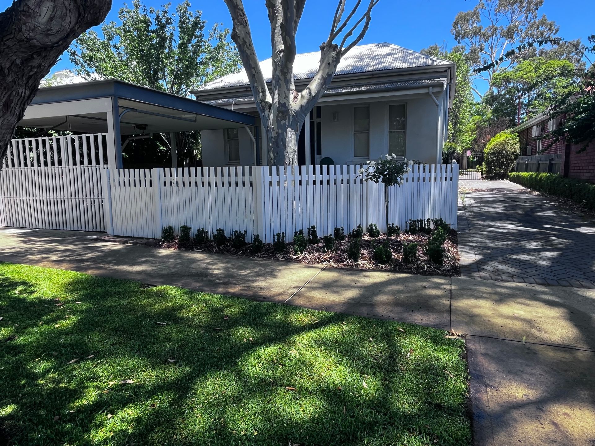 White house with matching fence, carport, and driveway; sunny day.