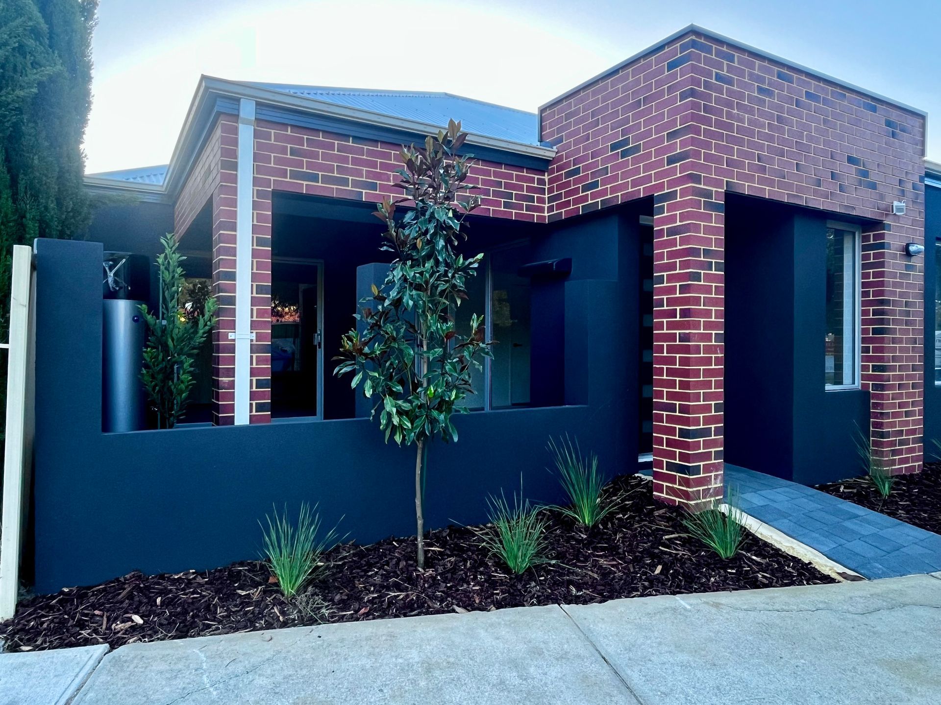 Modern brick and black house with a small tree and ramp.