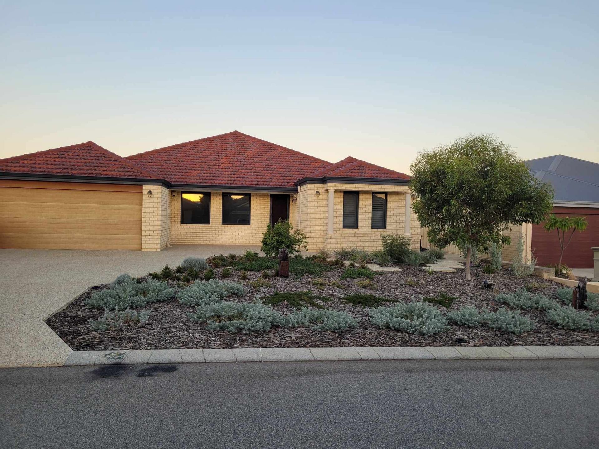 Beige brick home with red tile roof, small front yard garden, and wooden garage door.