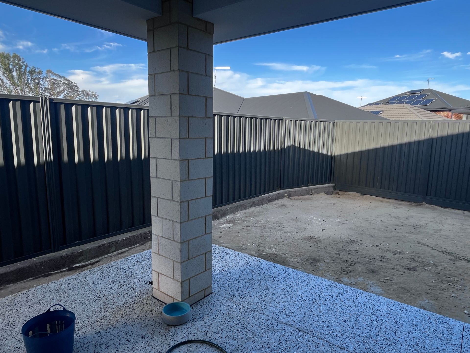 Concrete block pillar in an outdoor area with a gravel floor, bordered by a dark gray fence under a clear sky.