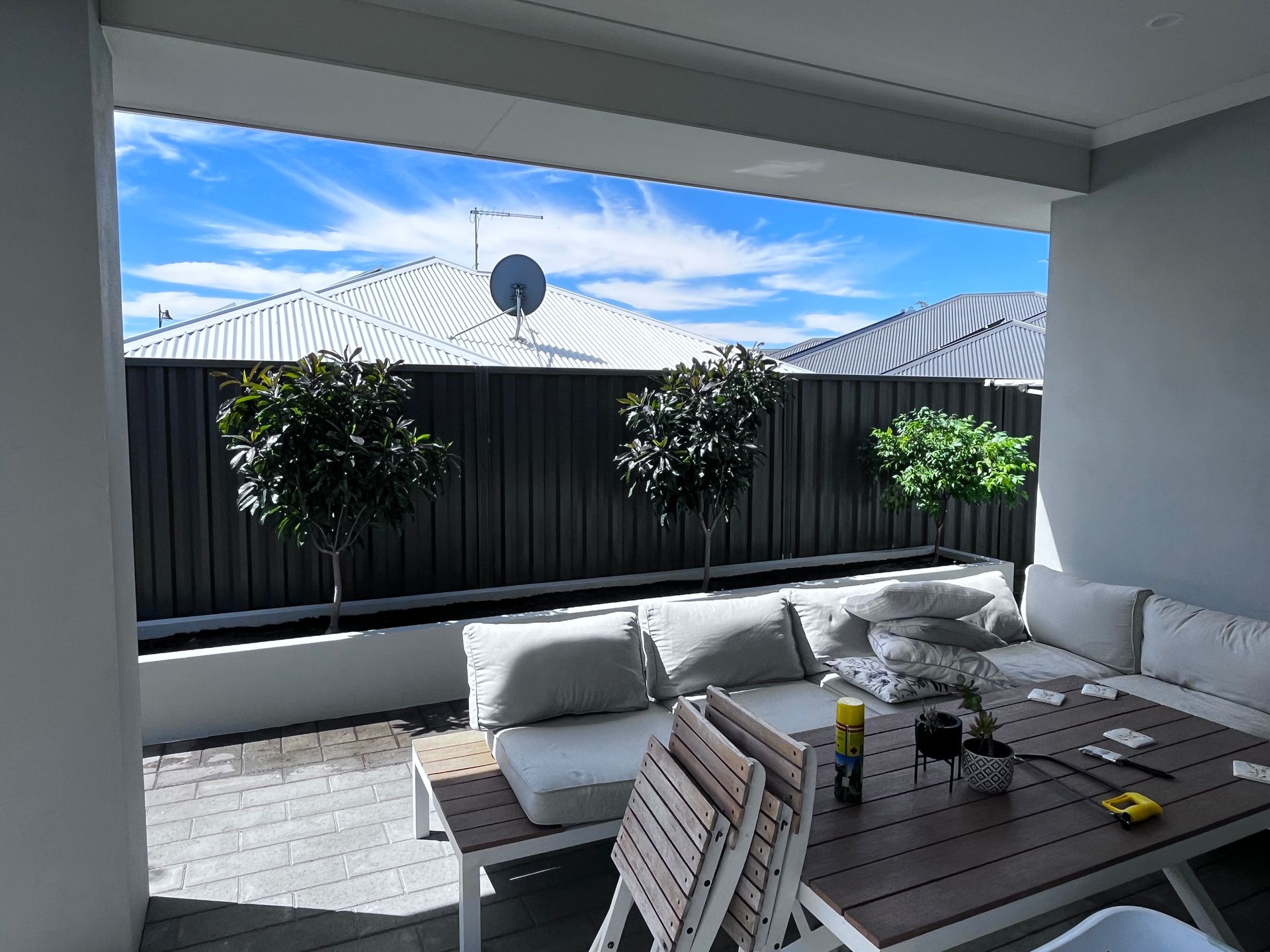 Patio with outdoor furniture, looking out at a fence, trees, and blue sky.
