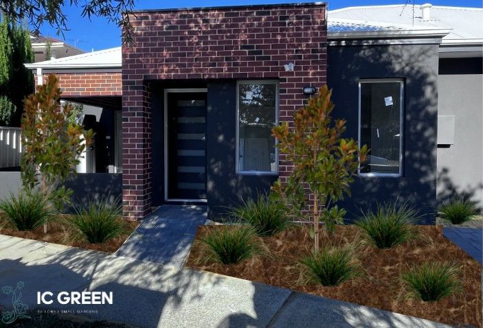Modern house with brick facade, dark grey walls, front garden with plants and mulch, sunny day.