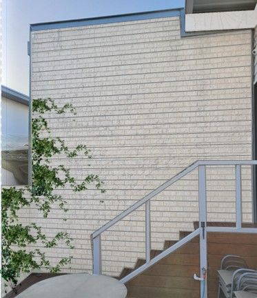 Exterior of a building with light-colored, horizontal siding, staircase with metal railing and a deck.