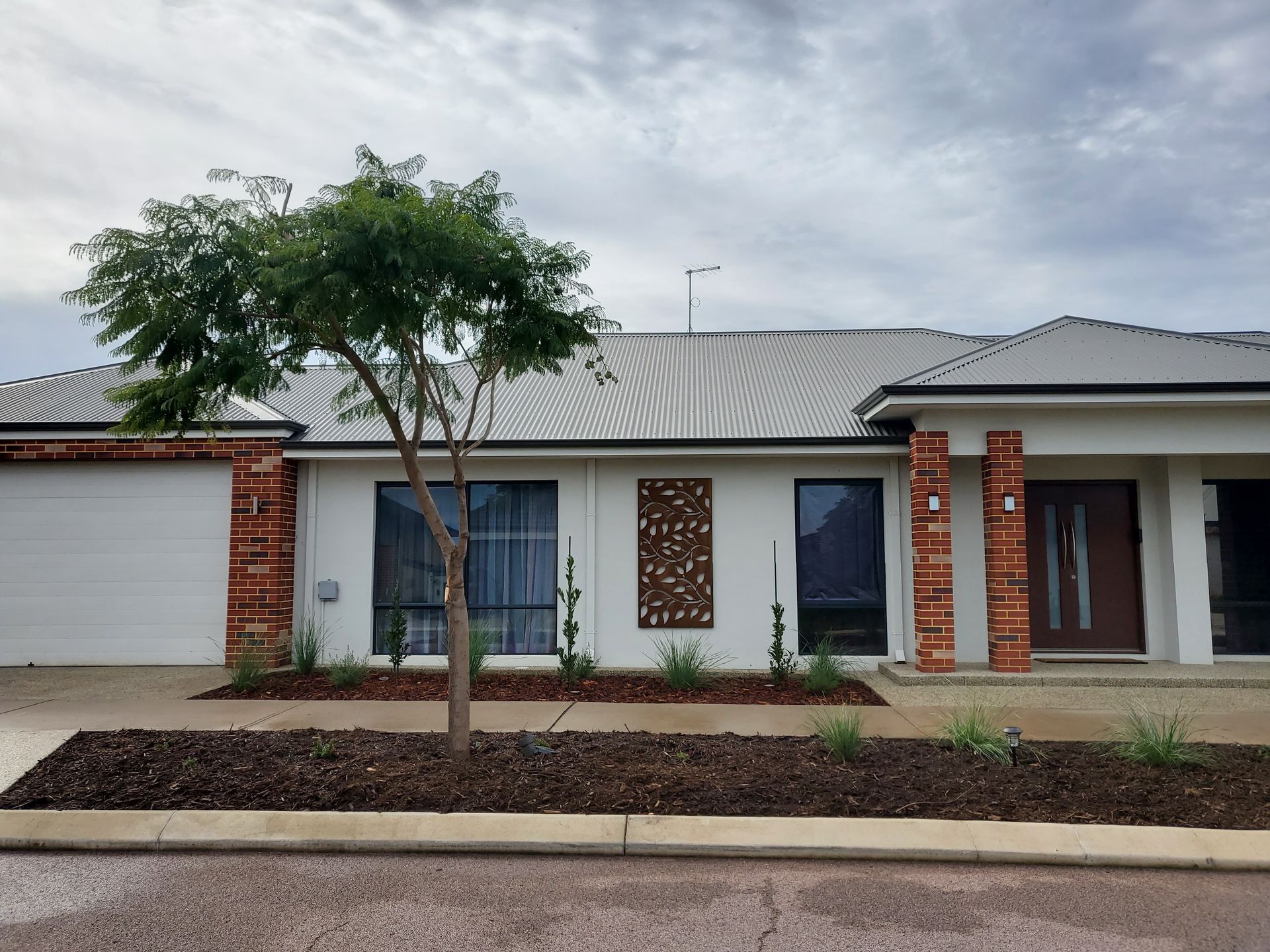 House with a white facade, brick accents, dark windows, and a tree in front, under a cloudy sky.