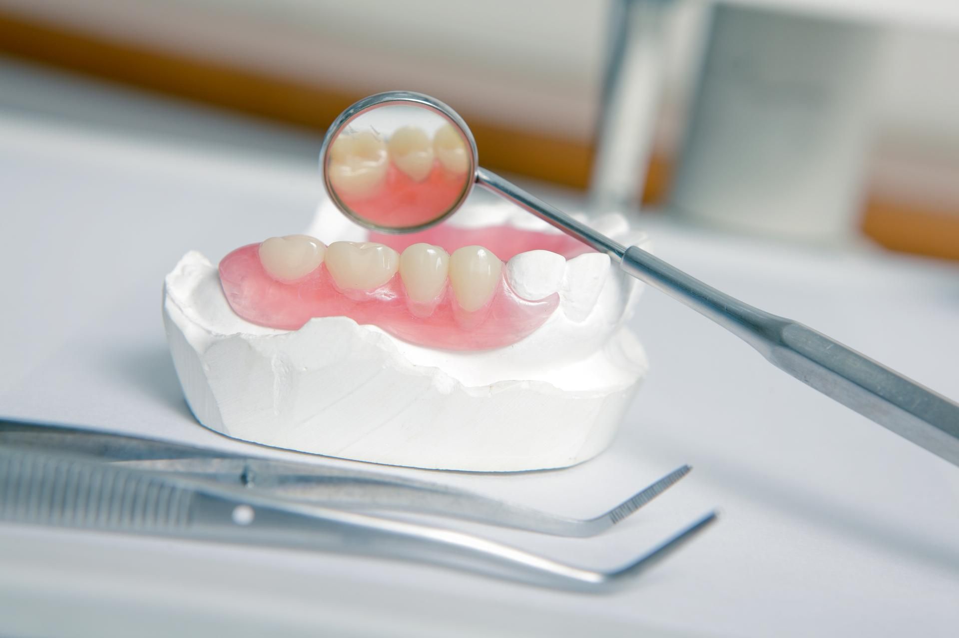Dentures on a mold with dental mirror and tools. Pink, artificial teeth in a dental setting.