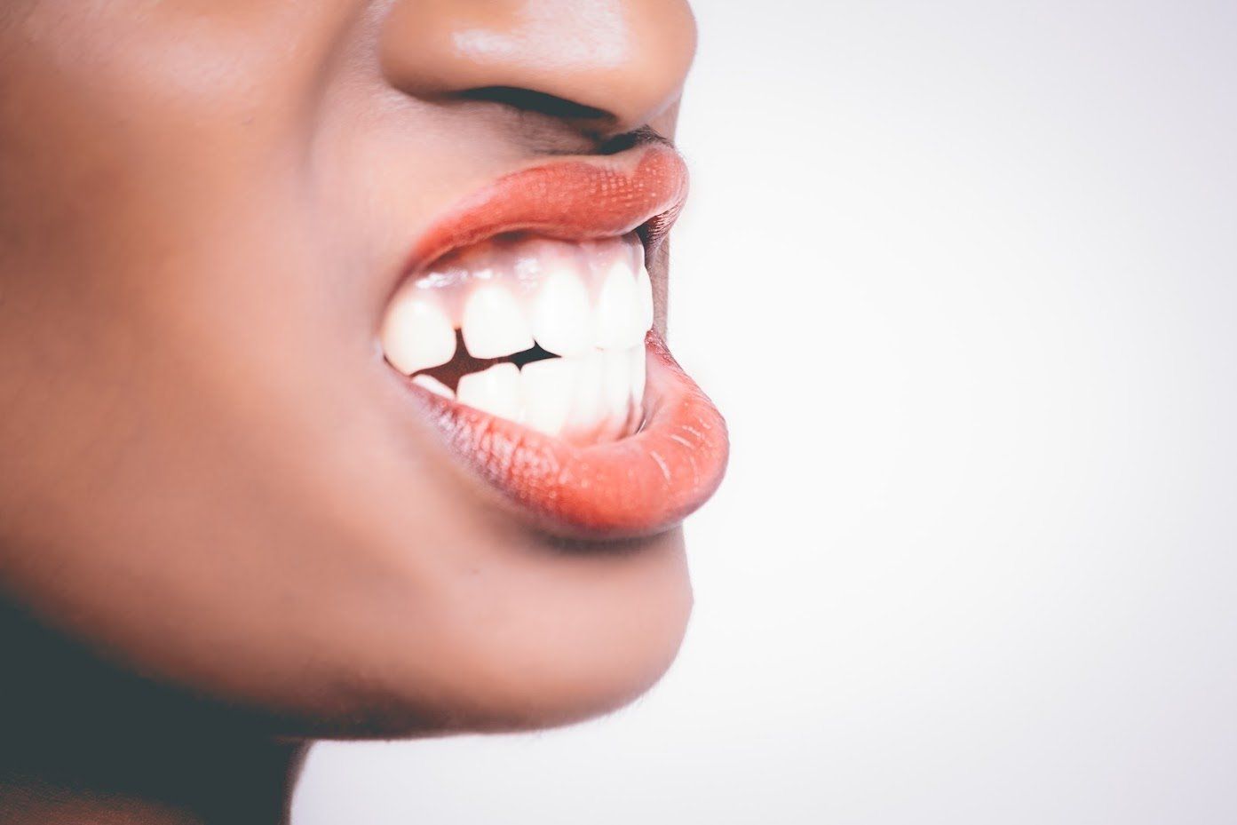 Close-up of mouth with teeth clenched, orange lipstick, against a white background.