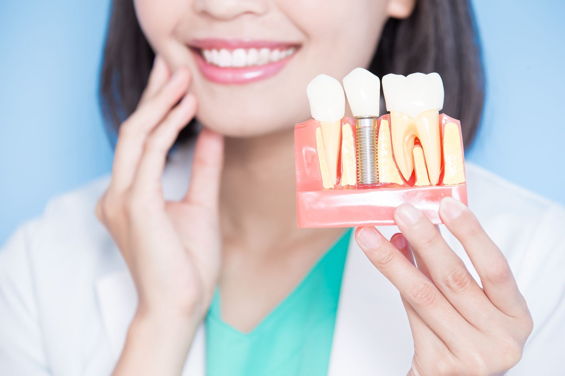 A person holding a dental model showing natural teeth and a dental implant with a metal screw.