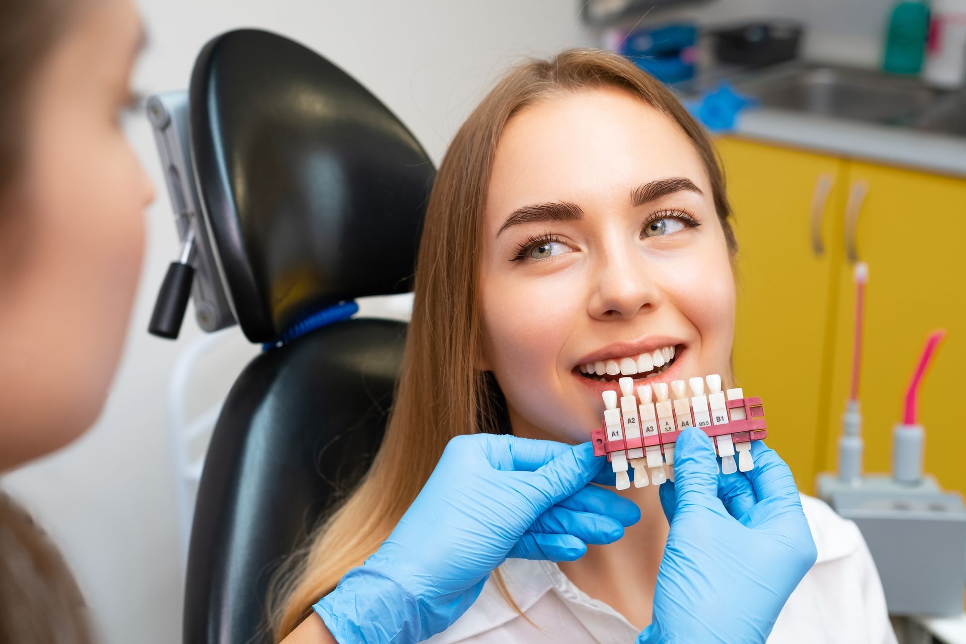 Woman in dental chair having teeth shade matched by a dentist.