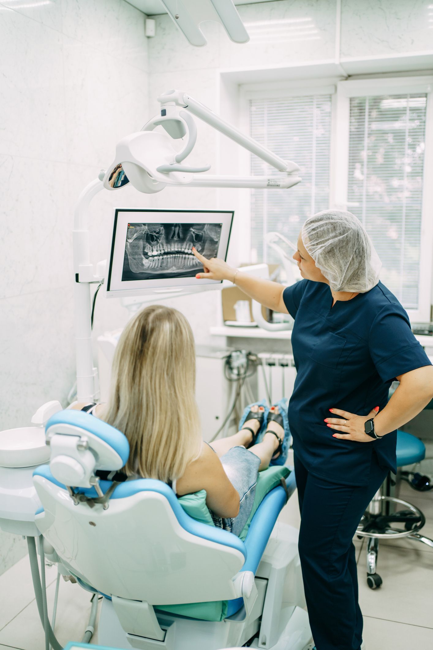 Orthodontist shows the patient an x-ray of the teeth and gives recommendations for treatment. Dentist pointing at x-ray for patient in dental chair, modern office.
