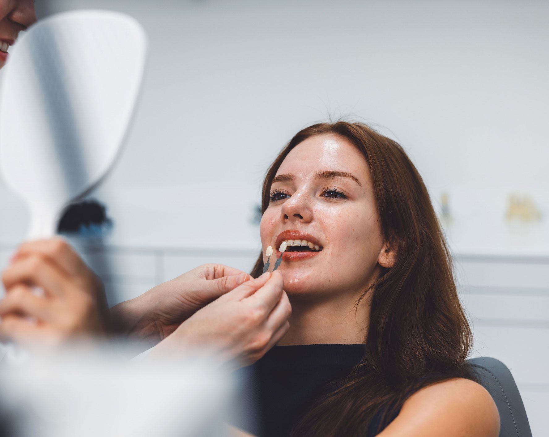 Woman having teeth color matched in a dental office. A dentist is holding a shade guide.