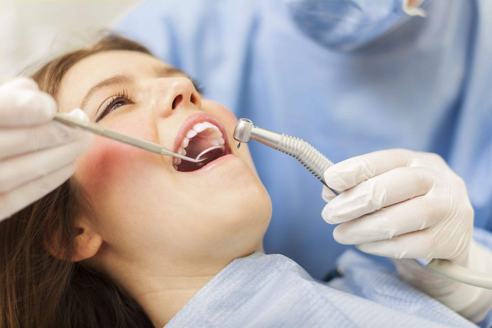 Woman in dental chair, mouth open, dentist with tools.