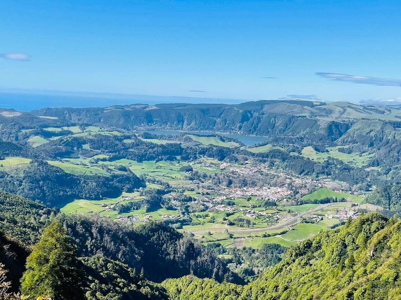 A wide-angle, high-altitude view of the Sete Cidades volcanic crater in the Azores, featuring a town and lake below.