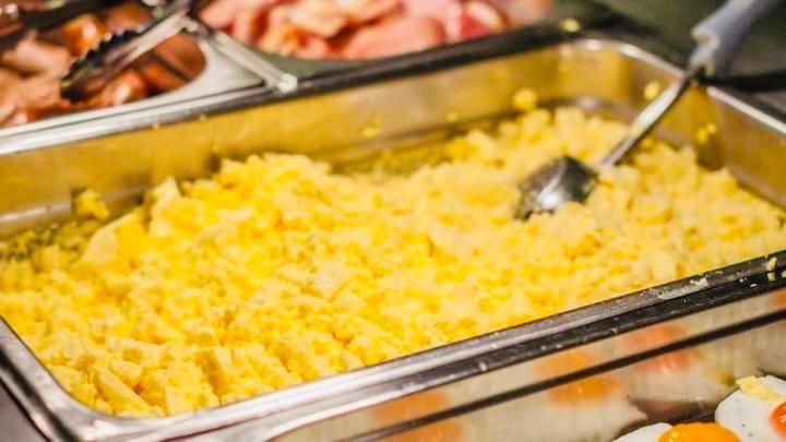 A metal buffet tray filled with fluffy yellow scrambled eggs, with a serving spoon resting inside.