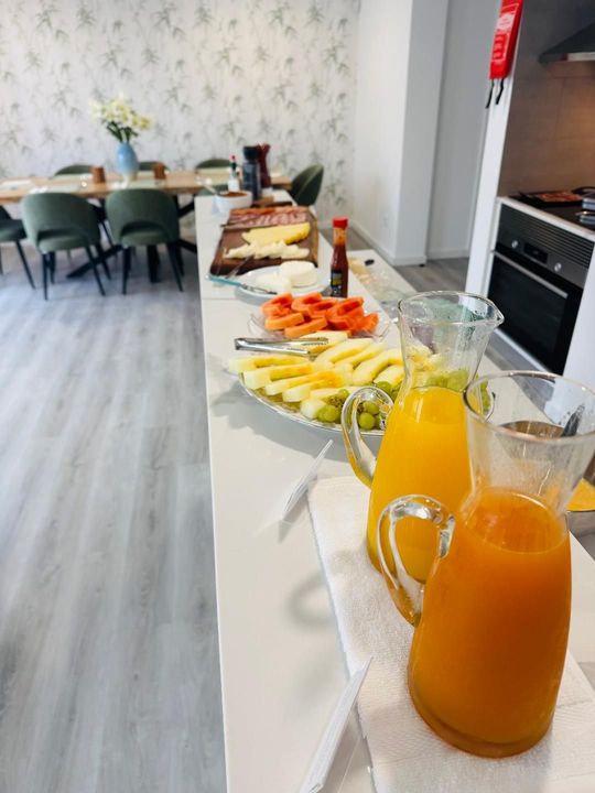 A breakfast buffet with pitchers of juice and platters of sliced fruit and cheese on a white counter in a dining room.