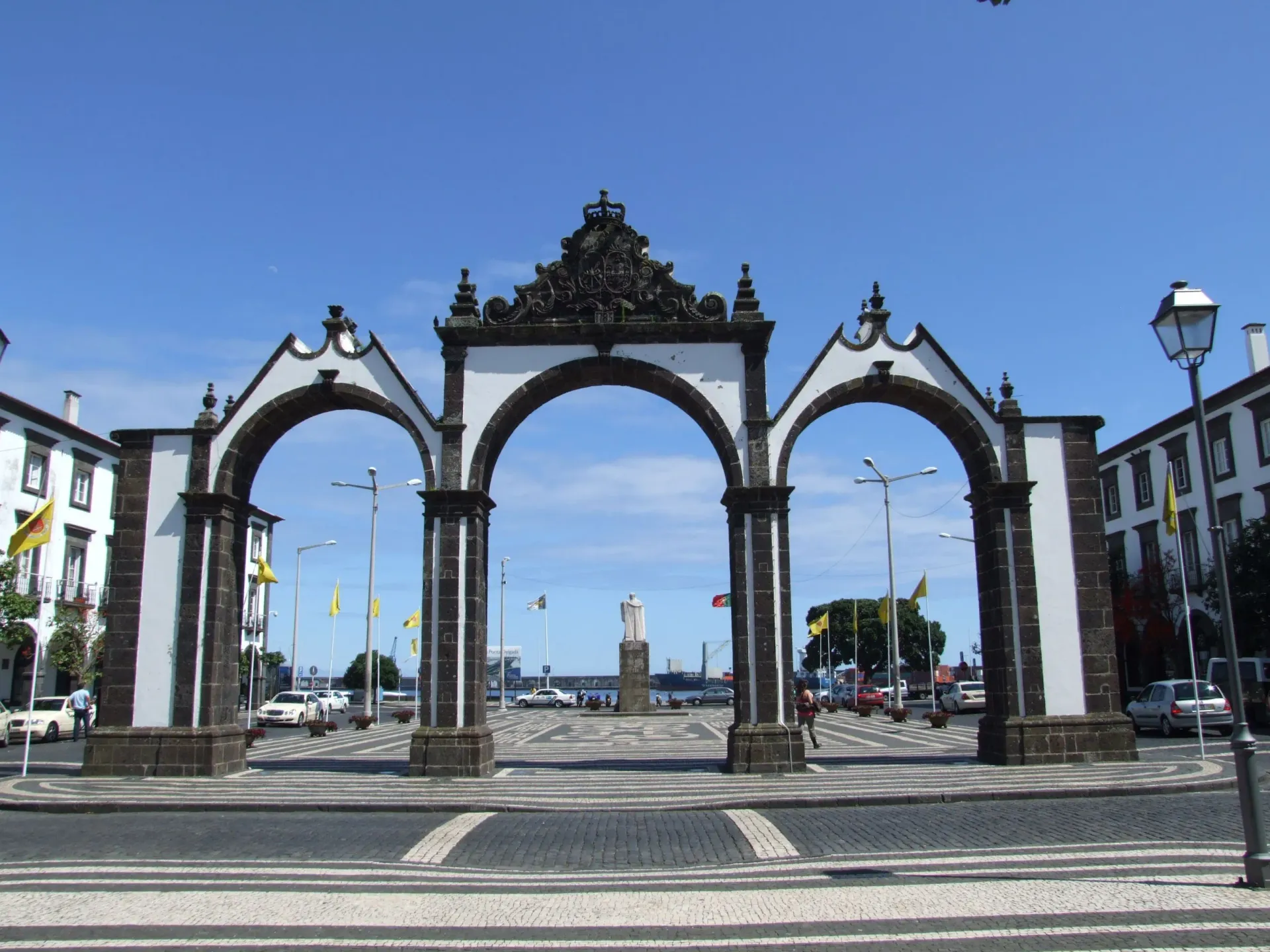 The Portas da Cidade, a historic three-arched gate with white plaster and dark stone, stands against a bright blue sky.