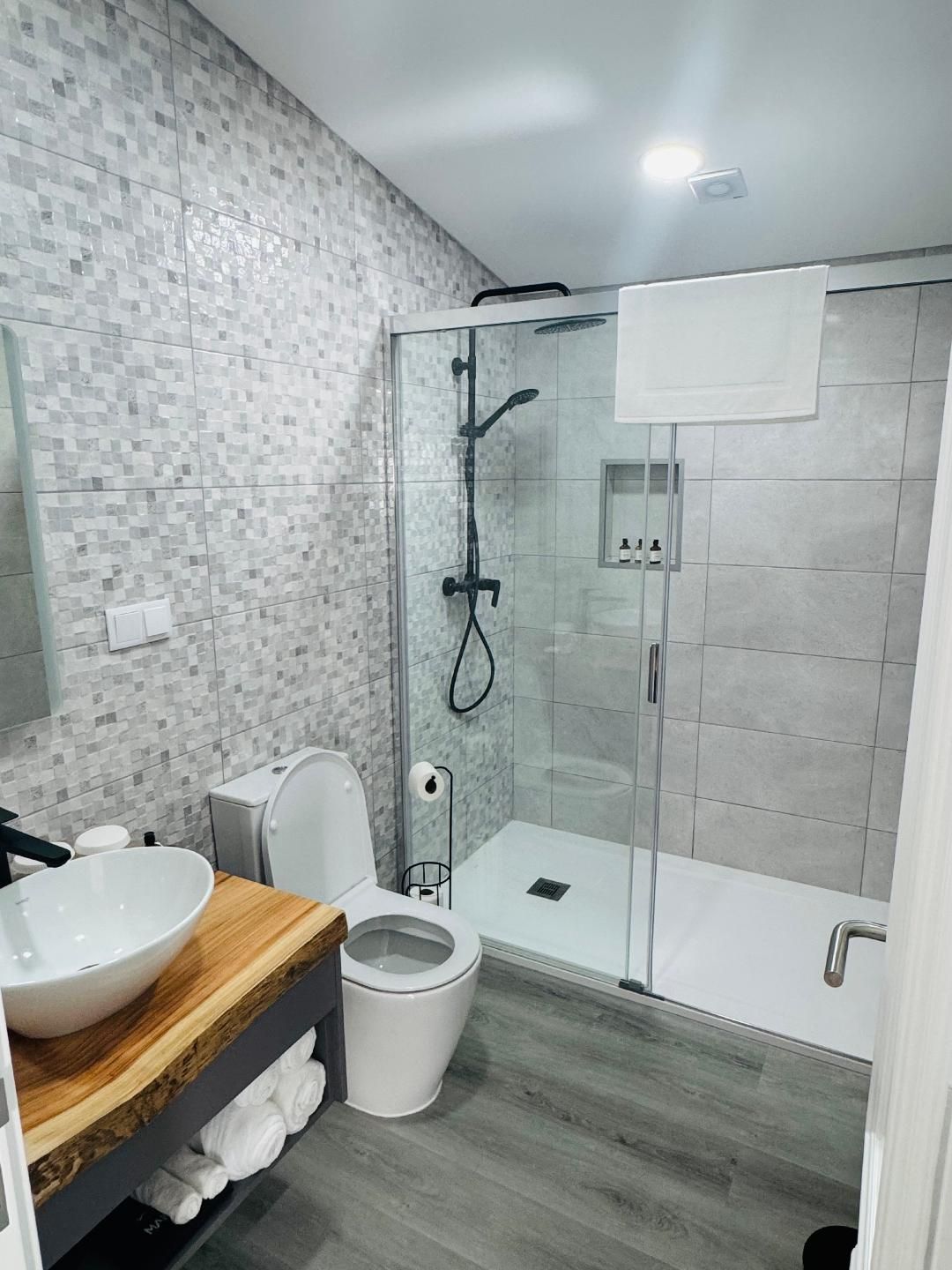 Modern bathroom with a white vessel sink on a rustic wood vanity, a toilet, and a glass-enclosed walk-in shower.