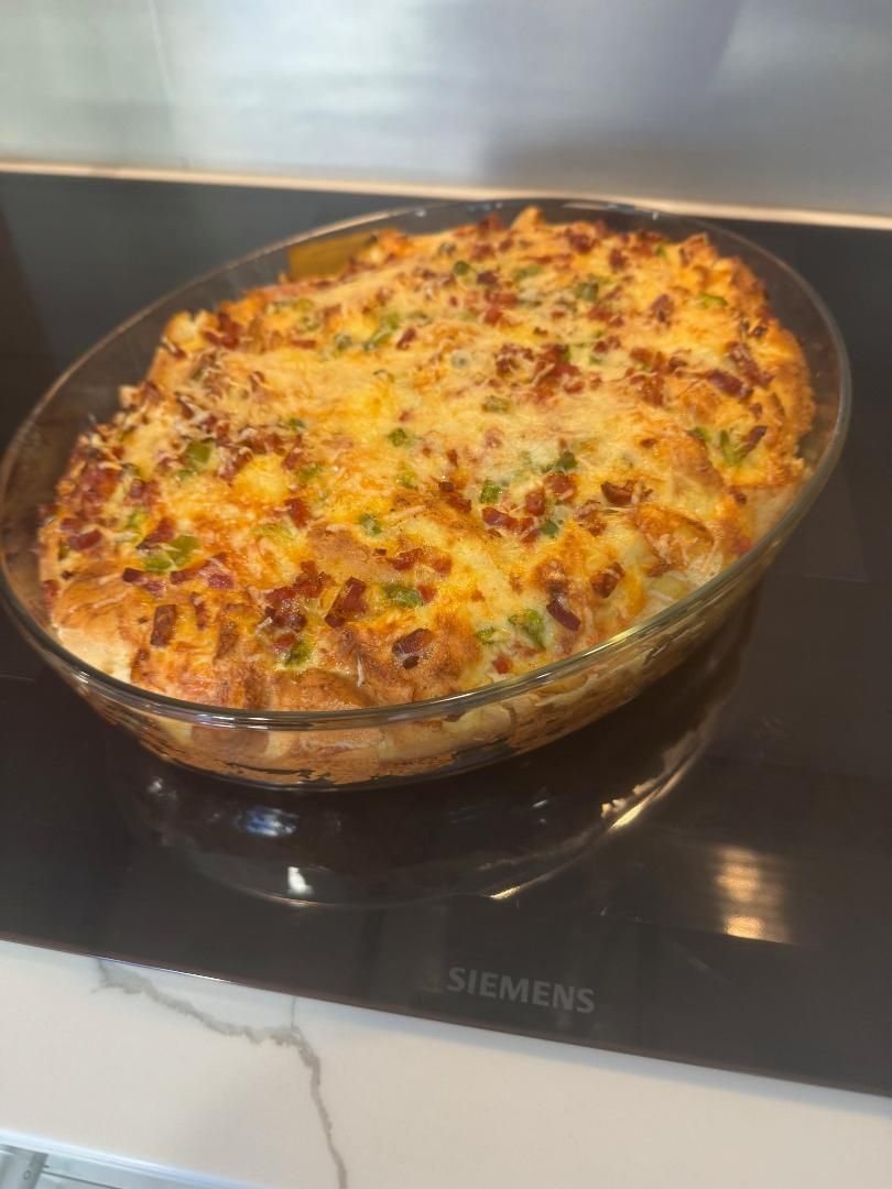 A golden-brown baked casserole with melted cheese and green bits in a glass dish sitting on a black stovetop.