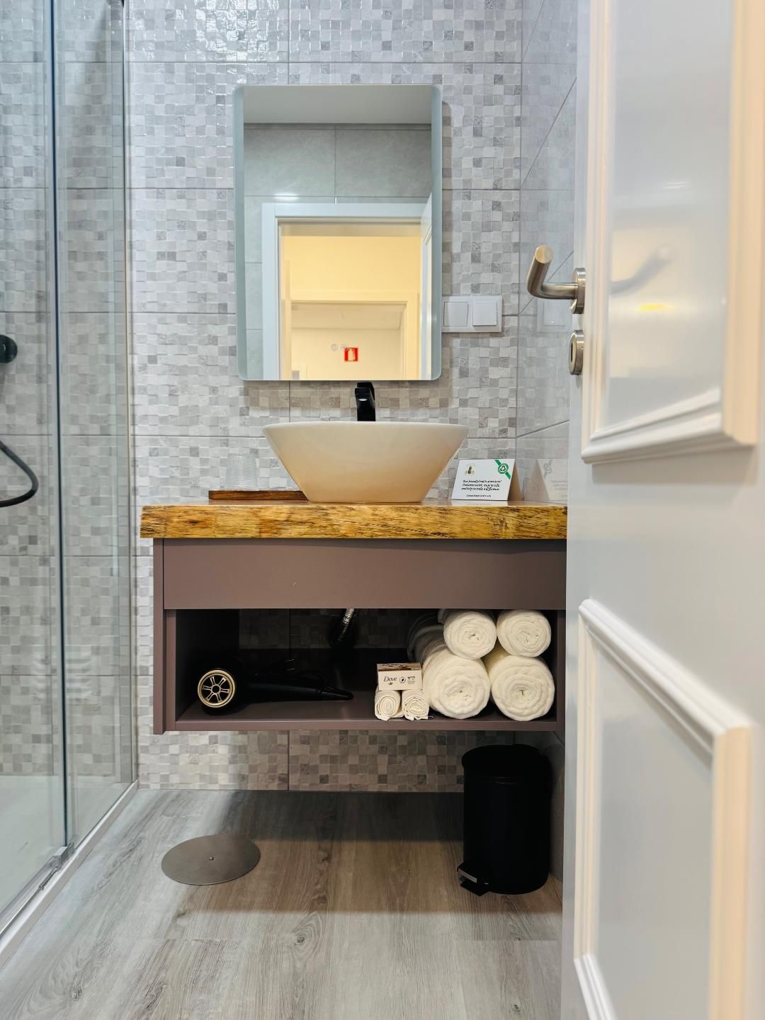 A modern bathroom featuring a vessel sink on a floating vanity with open shelving holding towels and a hairdryer.