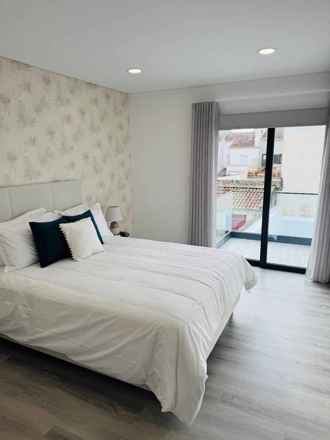 A modern bedroom featuring a bed with white bedding, navy and white pillows, and a floral wallpaper accent wall.