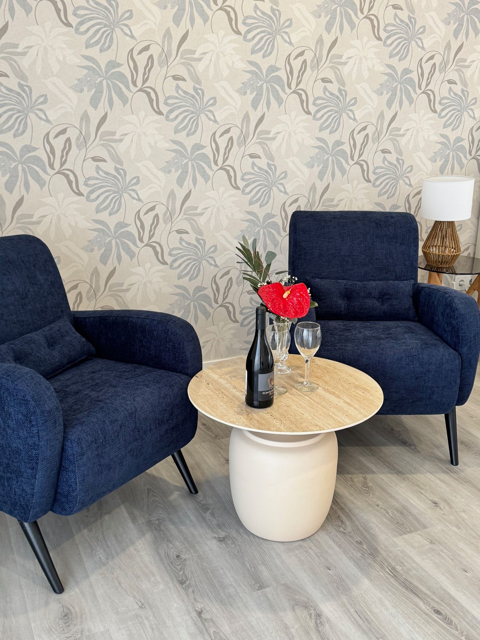 A living room with two chairs and a table with a bottle of wine on it.