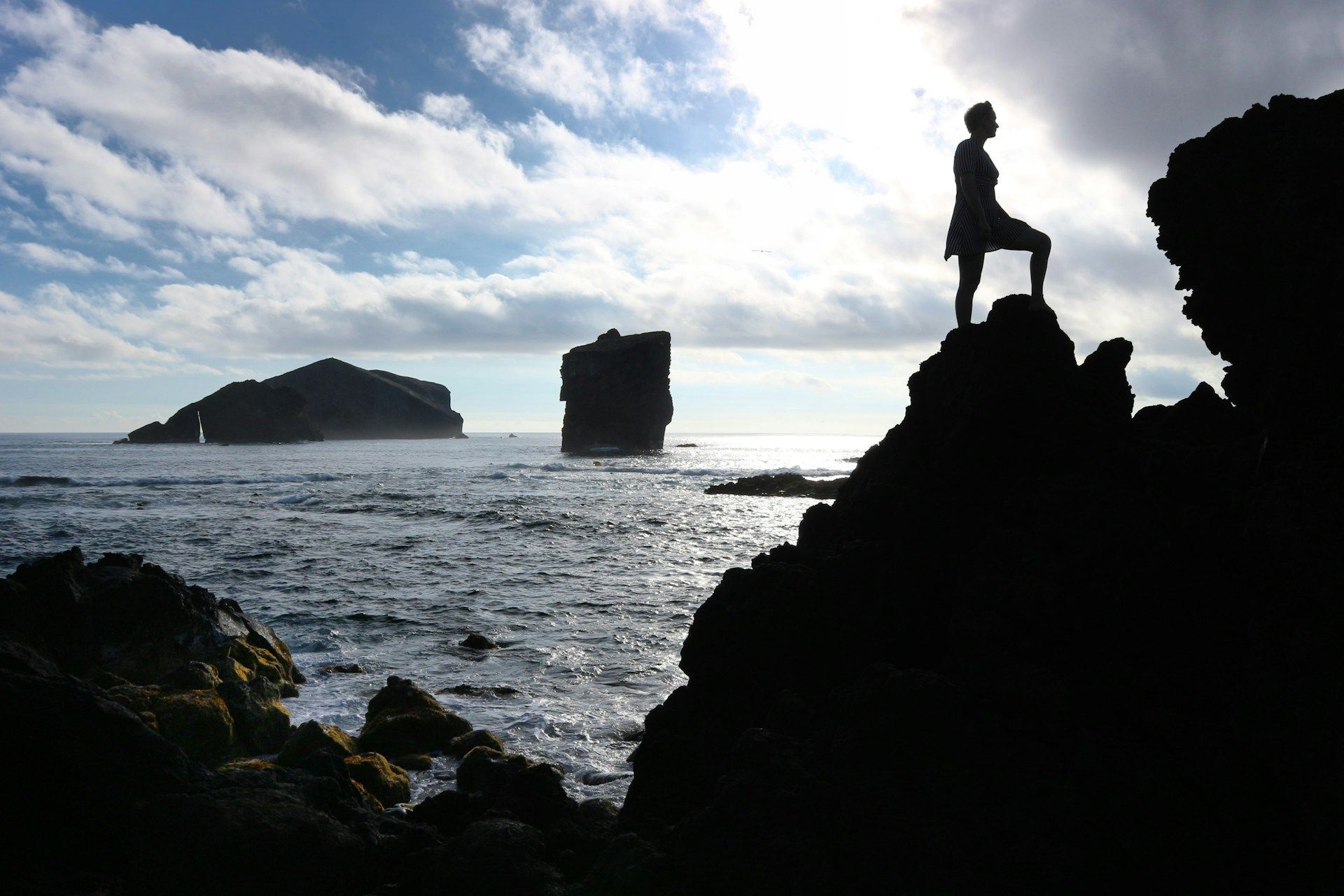 A silhouette of a person standing on a rock overlooking the ocean