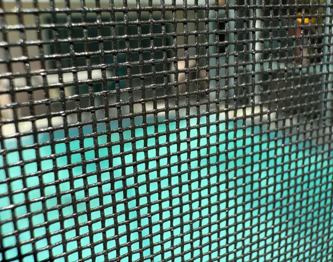 A view of a bright teal swimming pool seen through a dark, grid-patterned privacy or security screen.