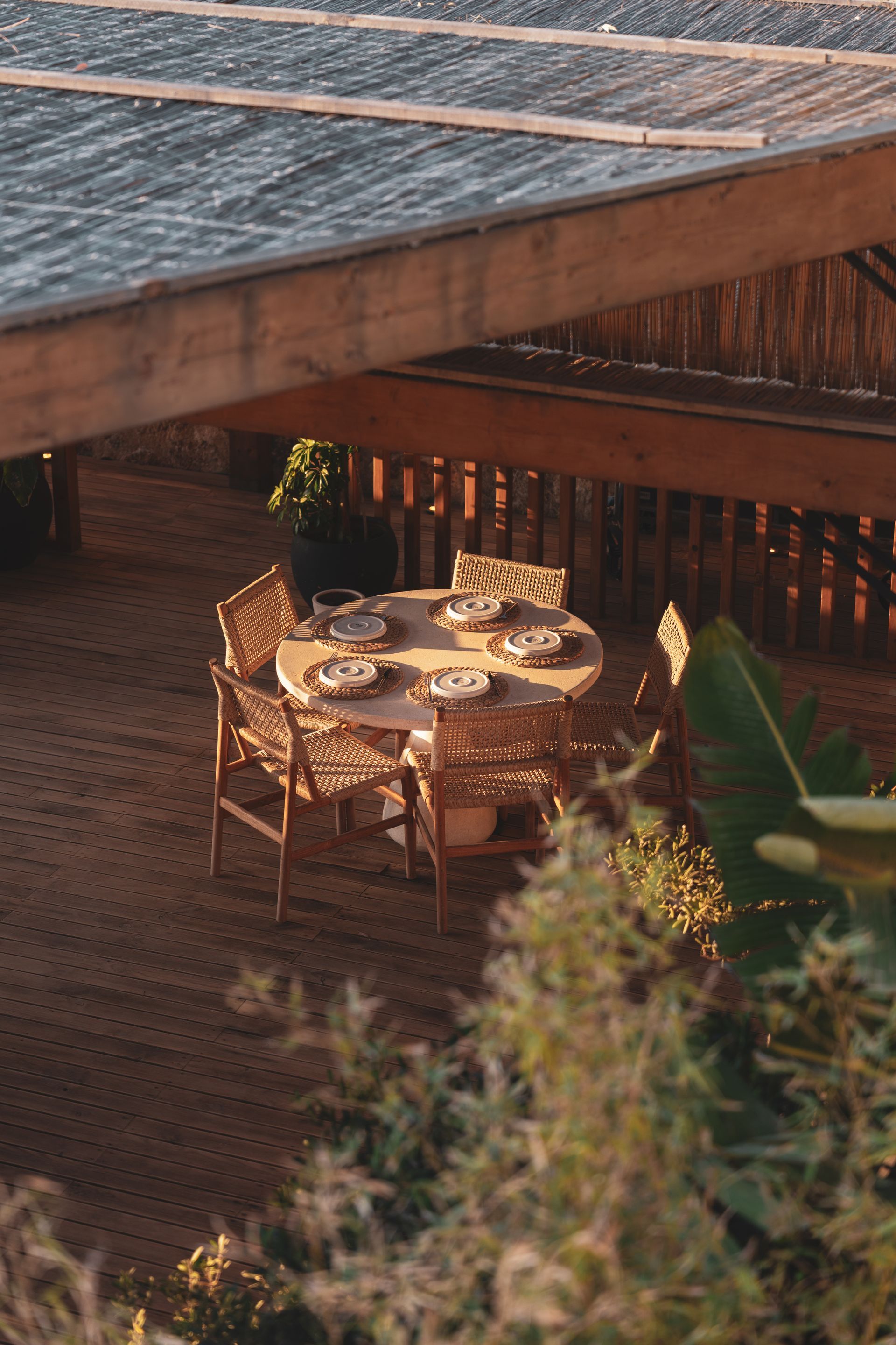 Elemanta Boutique Hotel Outdoor dining table with chairs under a wooden patio roof, lit by warm evening light.