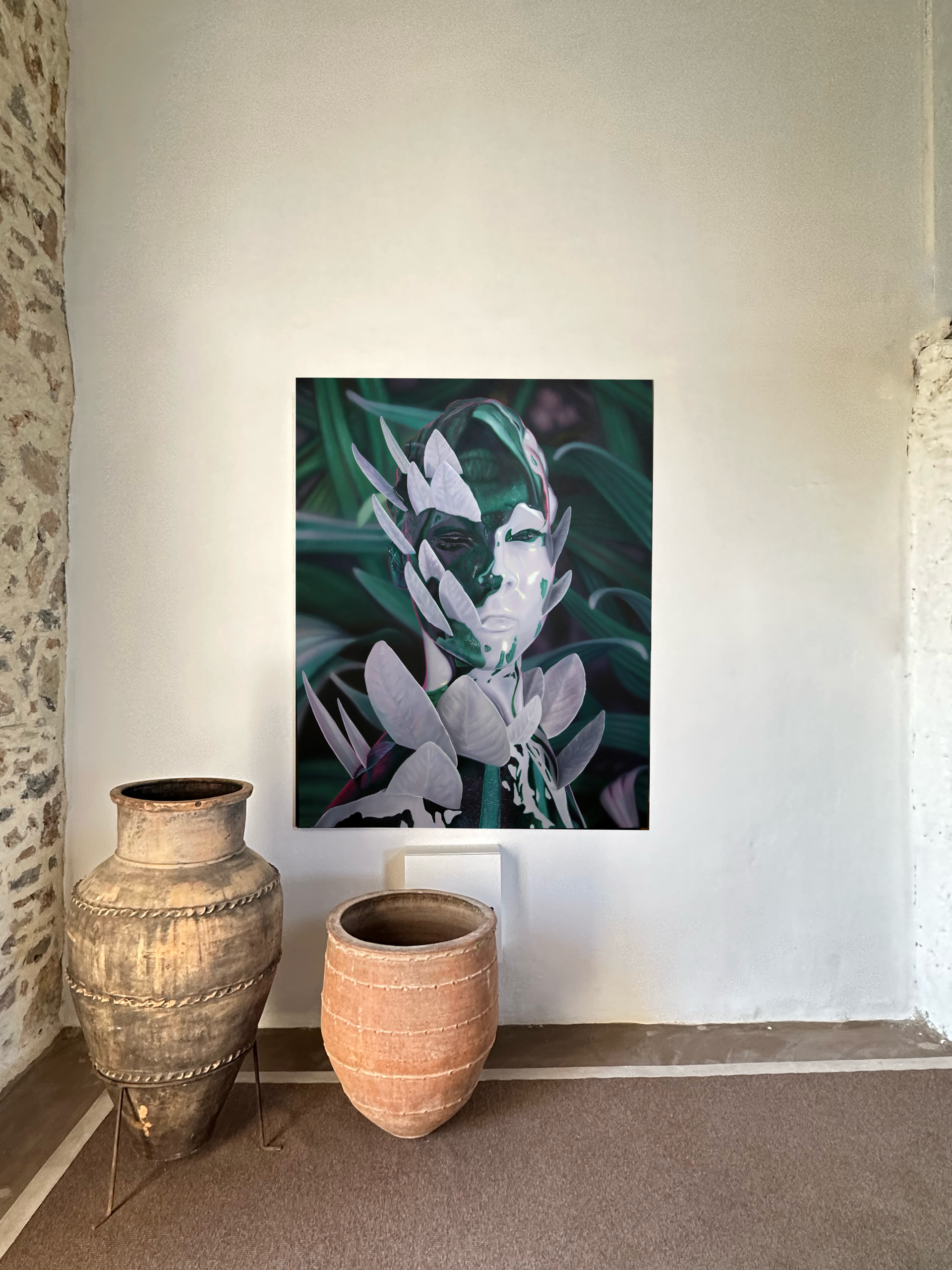 A large painting of a human face blended with foliage hangs on a white wall above two large, decorative clay urns.
