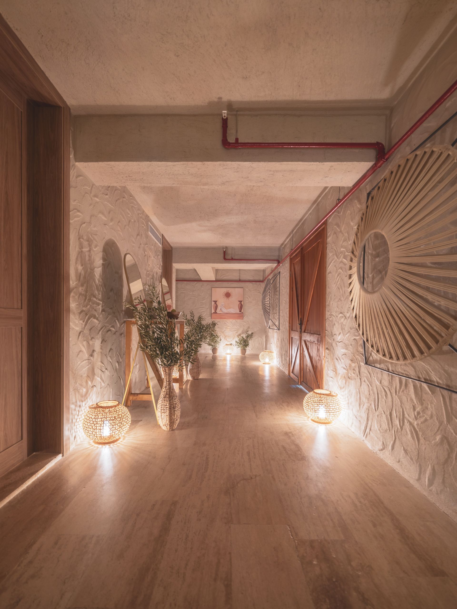 A softly lit hallway with textured walls, wood flooring, spherical lanterns, and a large decorative wall mirror.