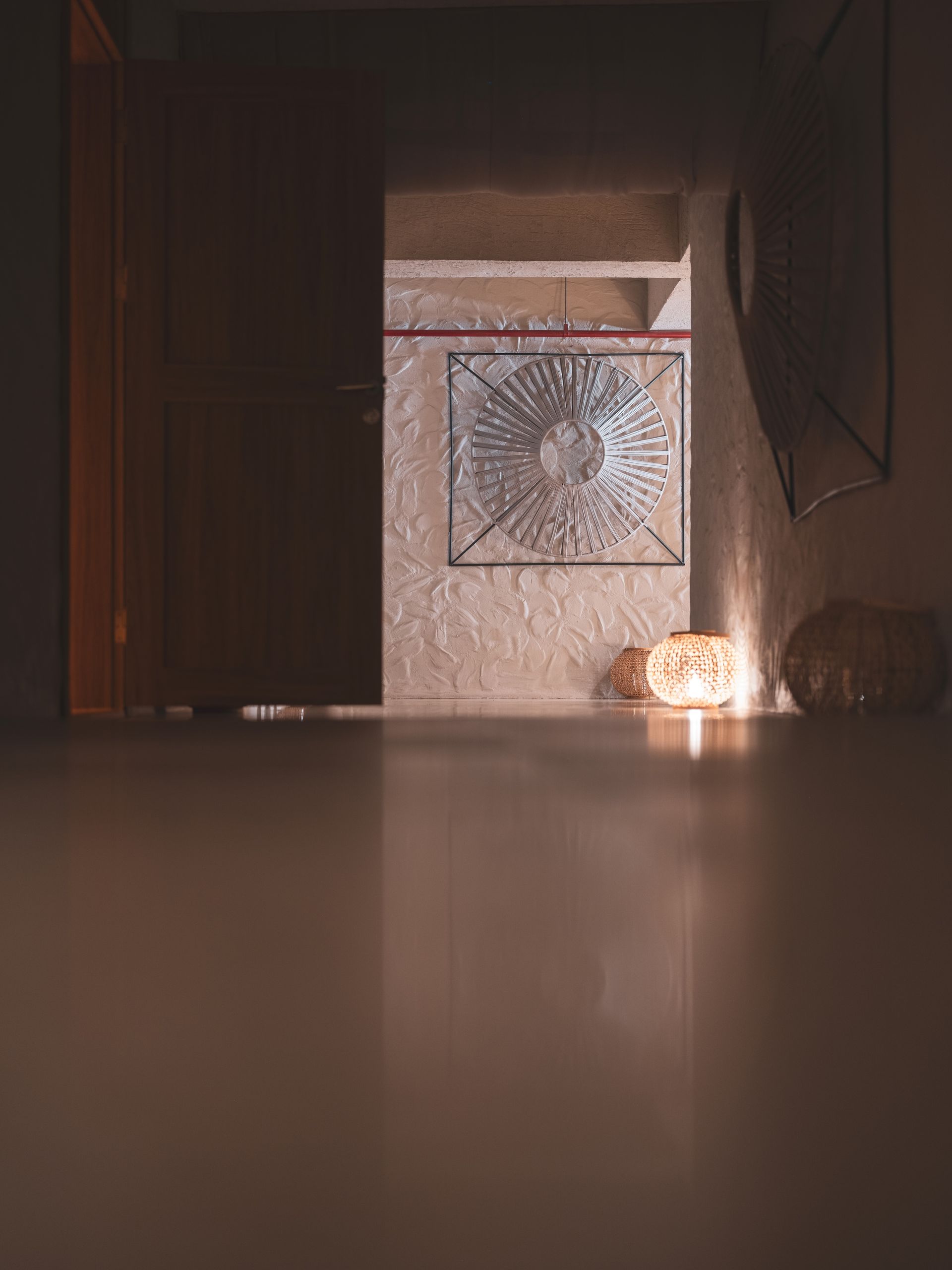 A glowing lantern sits on a dark hallway floor, illuminating a wall with a textured, circular metallic art piece.
