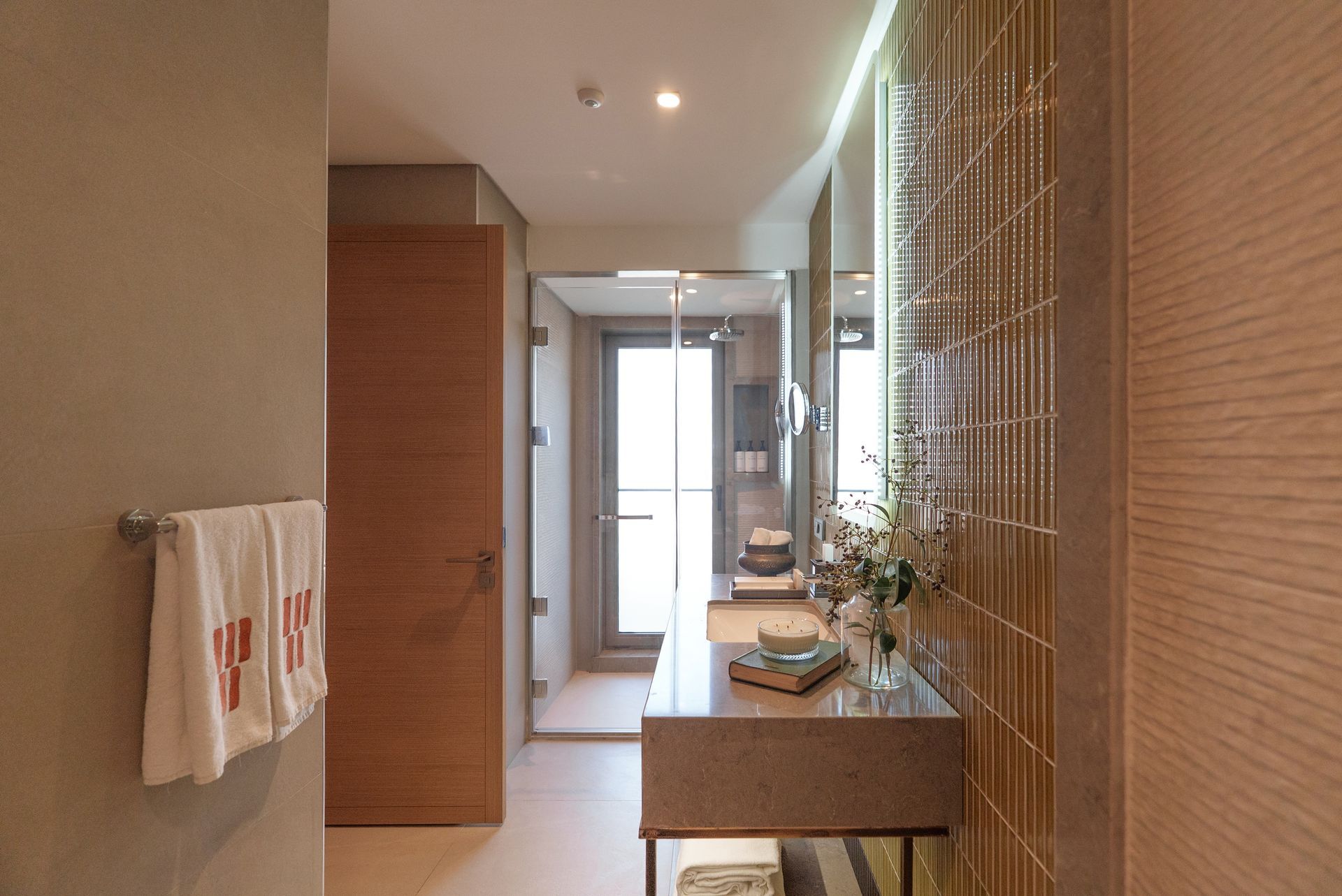 A modern bathroom with wood-toned walls, a floating vanity, a glass-enclosed shower, and a doorway leading to a balcony.