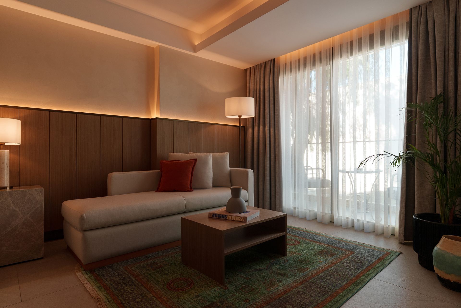 A cozy, modern living area with a beige daybed, red throw pillow, wooden coffee table, and soft ambient lighting.
