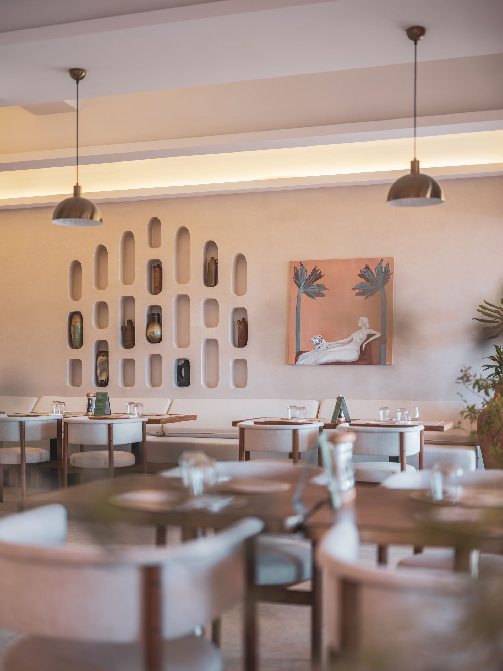 Modern restaurant interior with white chairs, wooden tables, a decorative niche wall, and a framed painting.