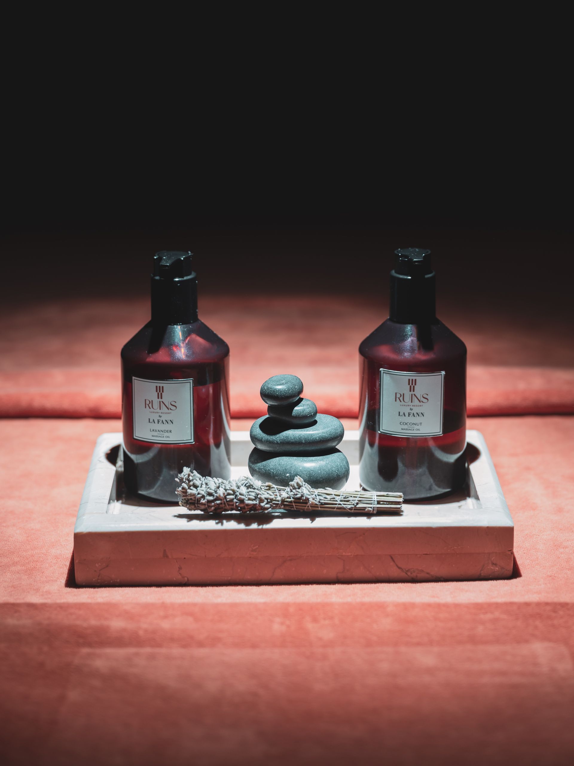 Two amber bottles and a stack of small gray stones on a light tray, set against a dark background on a red surface.