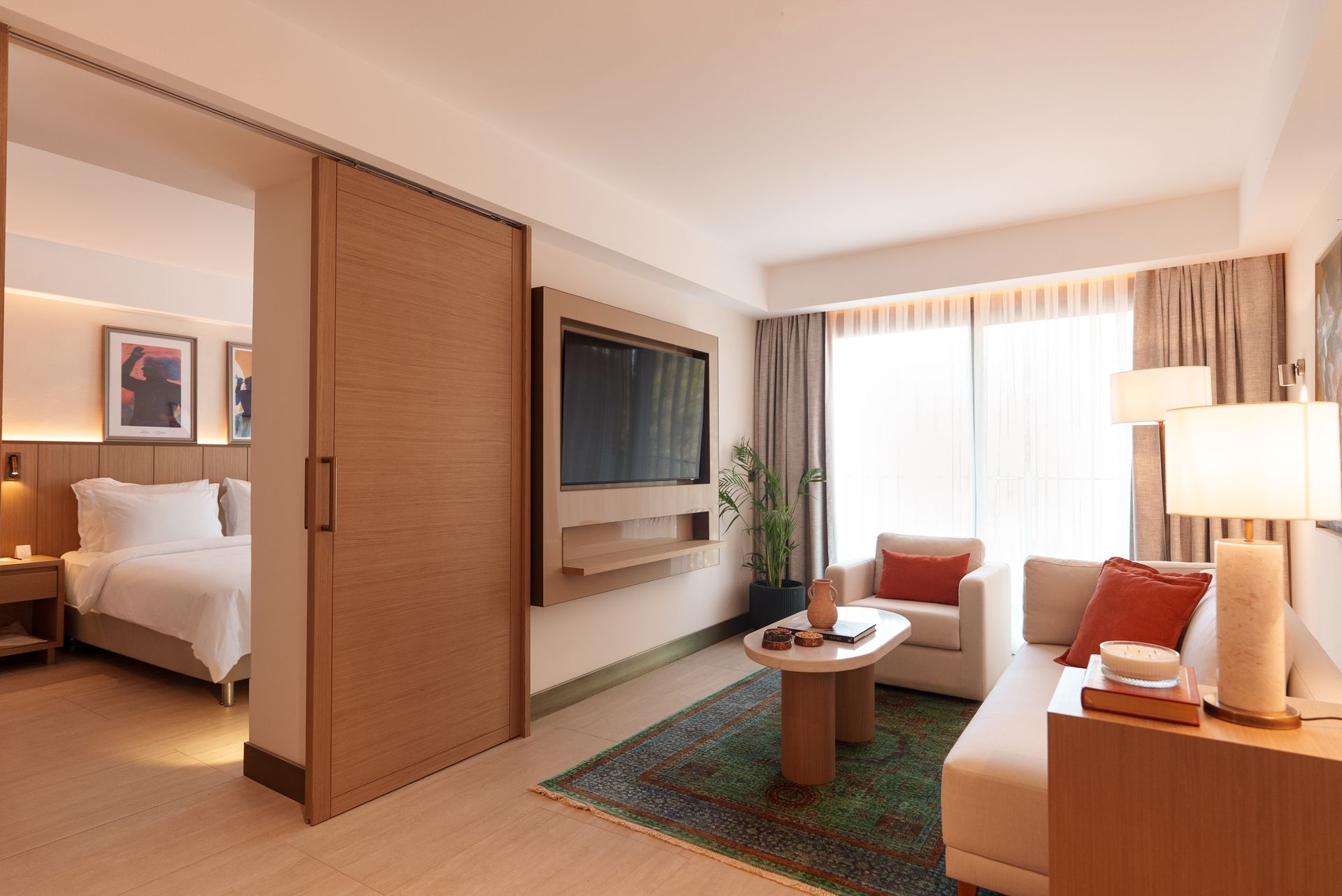 A hotel suite featuring a bedroom with a bed and a living area with a sofa, TV, and coffee table.