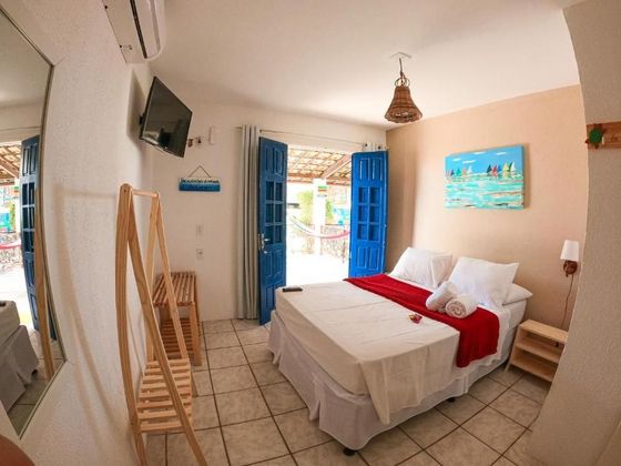 Quarto com cama, TV e portas azuis abertas que dão para um pátio.