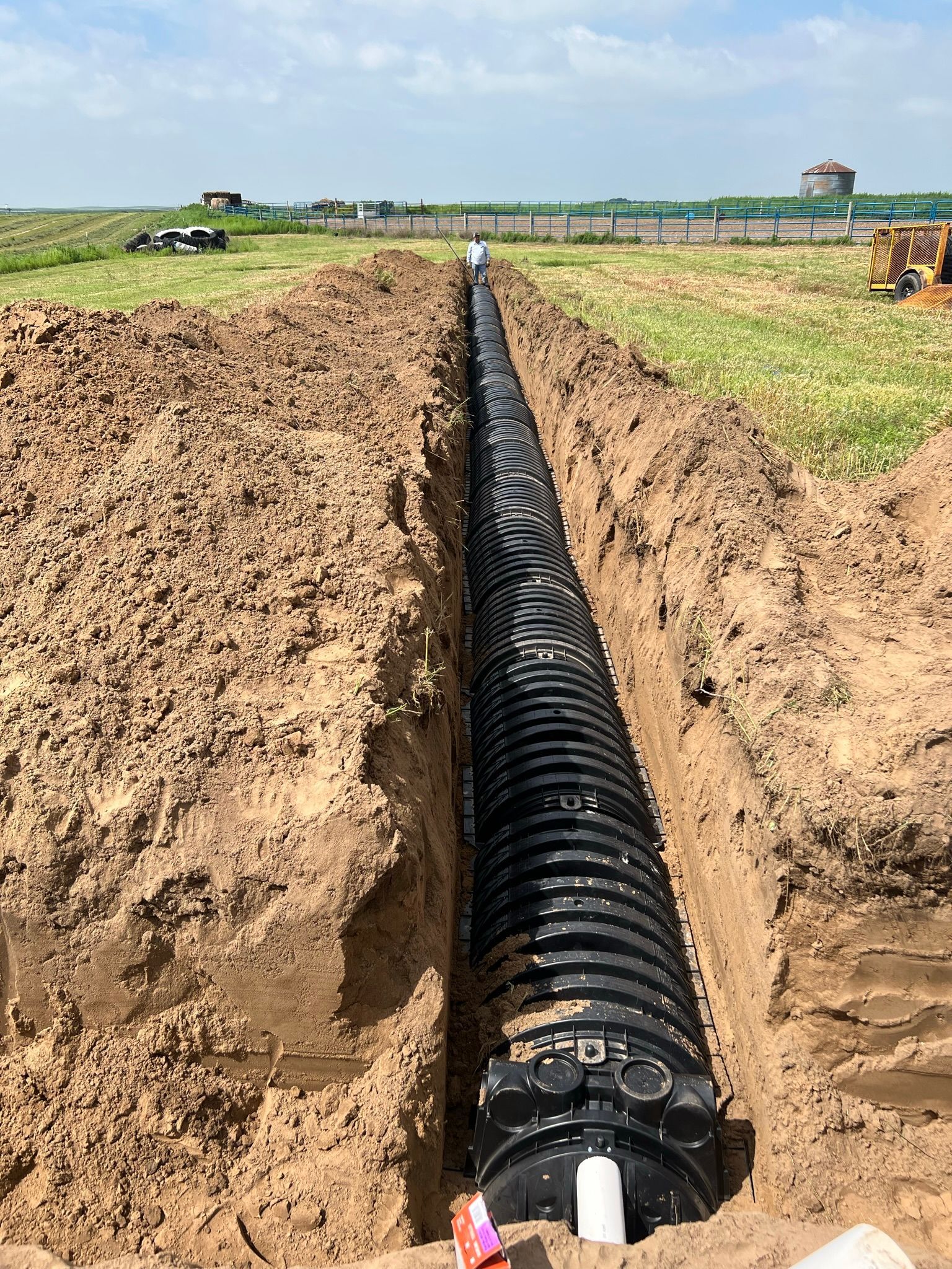 A long, black, corrugated pipe laid in a trench in a field.