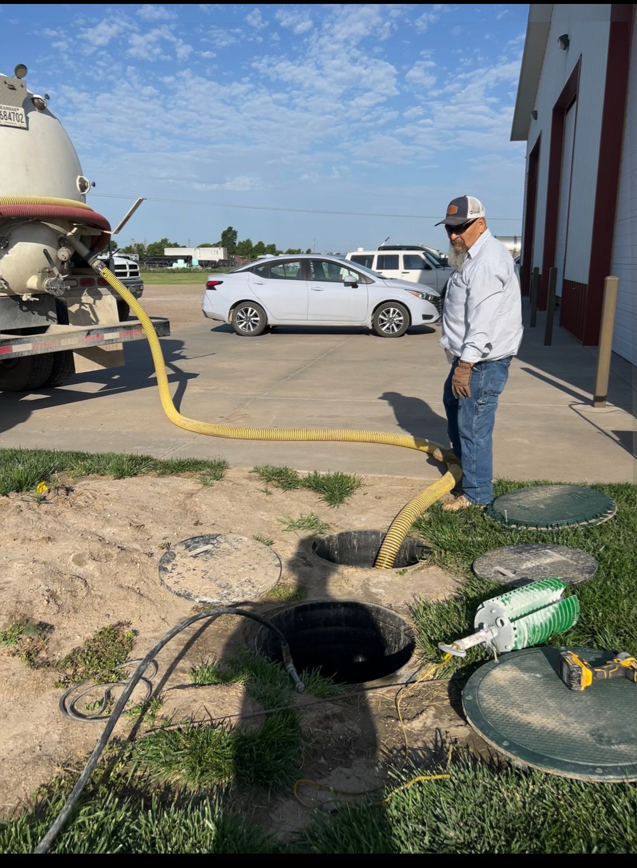 A man pumping septic tank waste from open ground covers into a tanker truck.