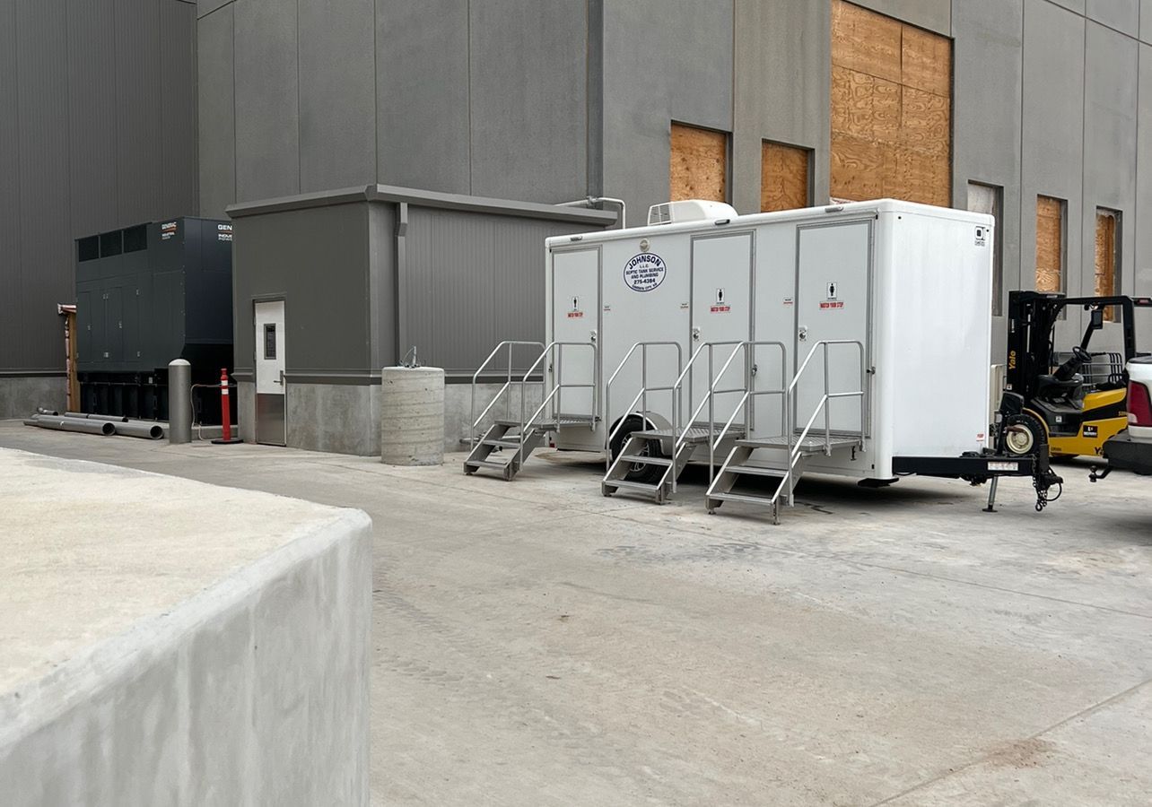 Portable toilets with stairs near a building under construction, next to a generator.