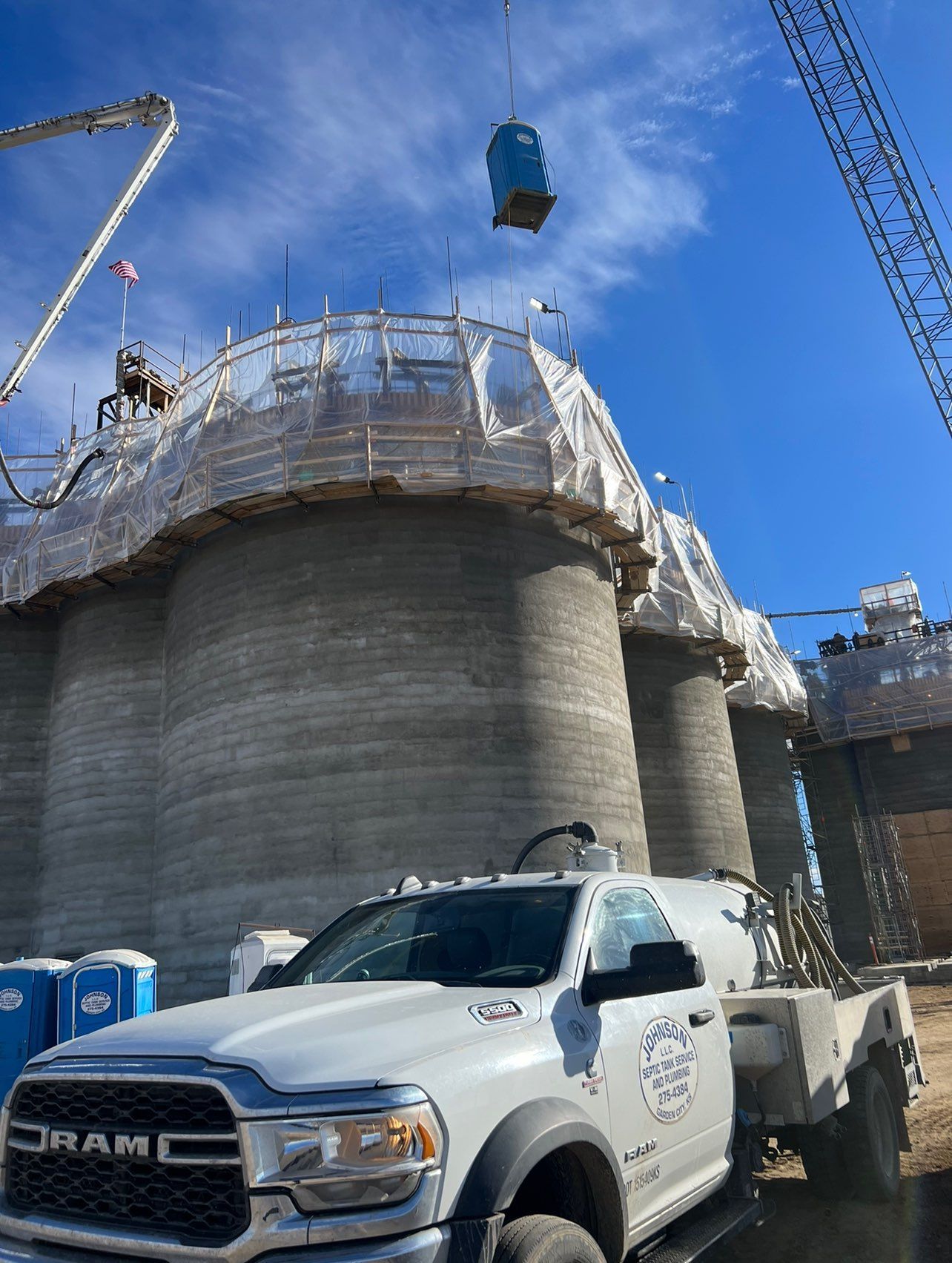 Construction site with 3D-printed concrete structures. A truck, crane, and porta-potty are visible under a blue sky.