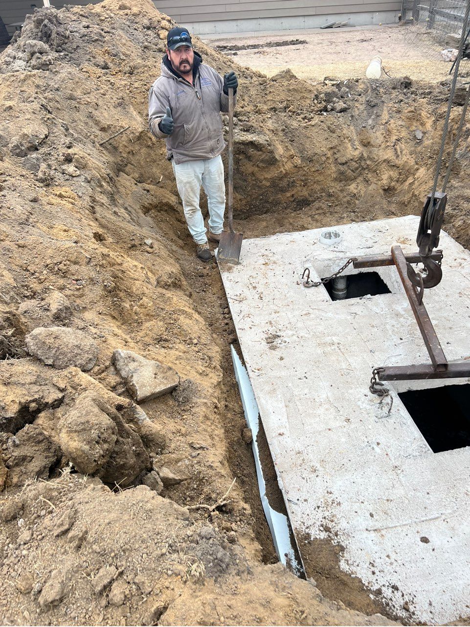 Man standing by an excavated concrete septic tank, holding a shovel.